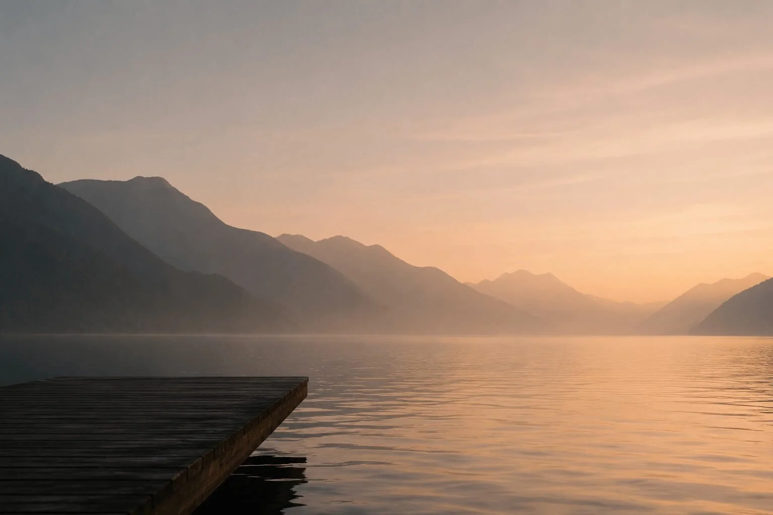 A tranquil lake at sunset with a wooden dock on the left, misty mountains in the background, and a soft pastel sky.