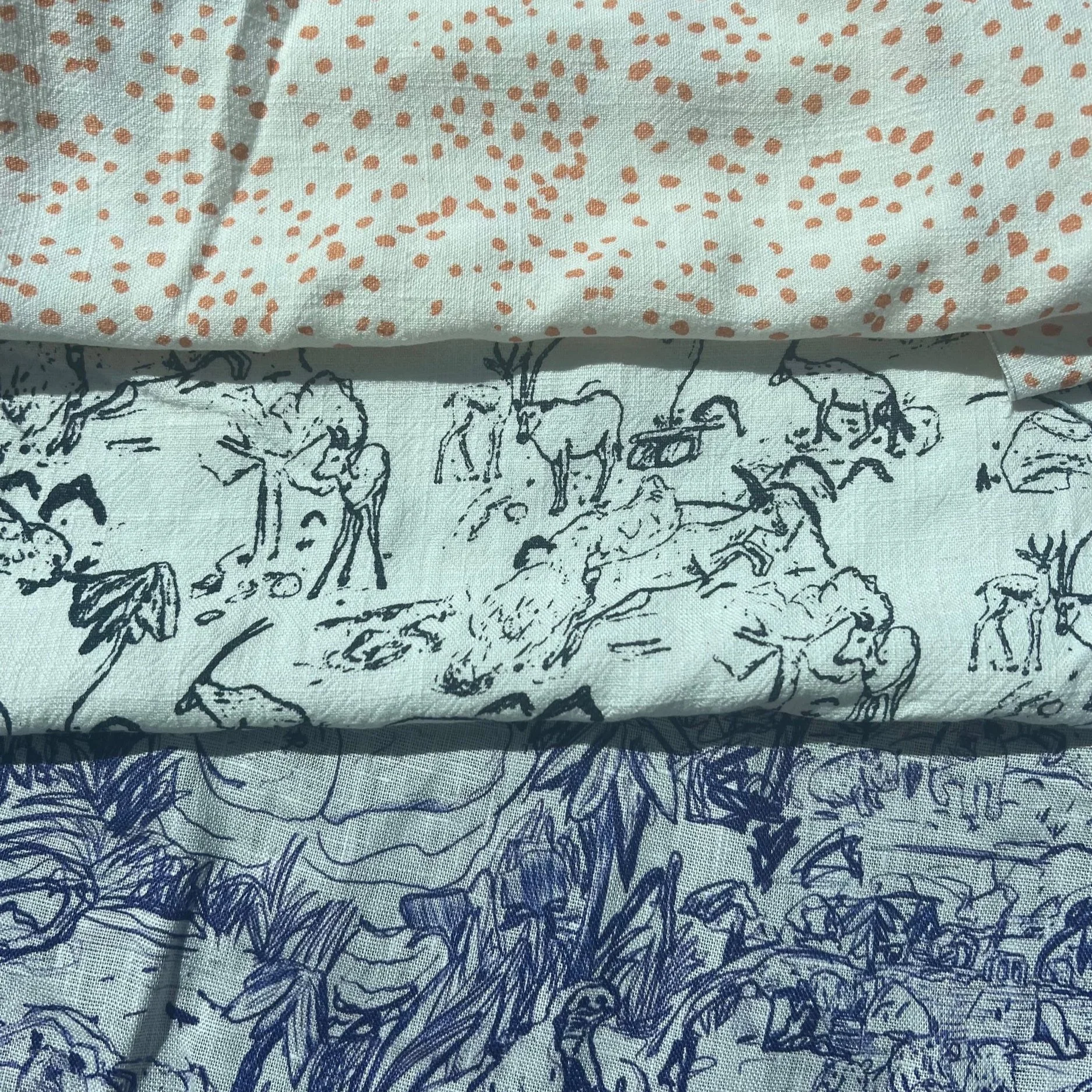 Close-up view of fabric with artistic black line drawing of horses and a layer of light green fabric with peach-colored polka dots on top.