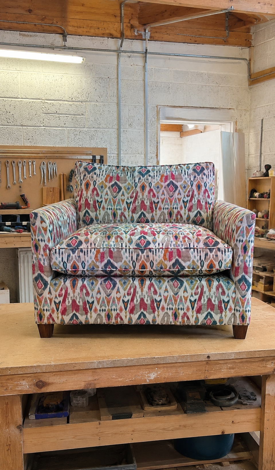 Colorful patterned upholstered loveseat sofa on a wooden worktable in a workshop.