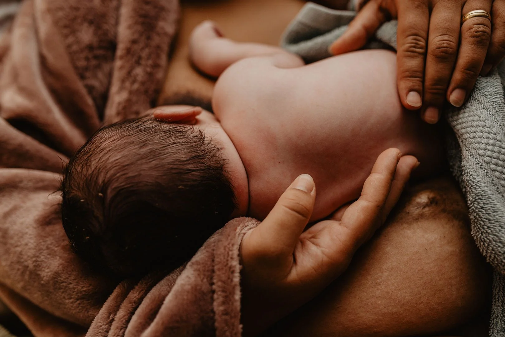 Close-up of a baby breastfeeding, held gently by an adult hands.