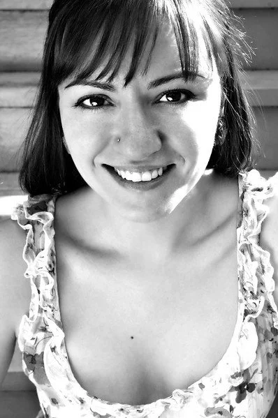 Black and white photo of a smiling woman with straight hair and a nose piercing, wearing a floral top.