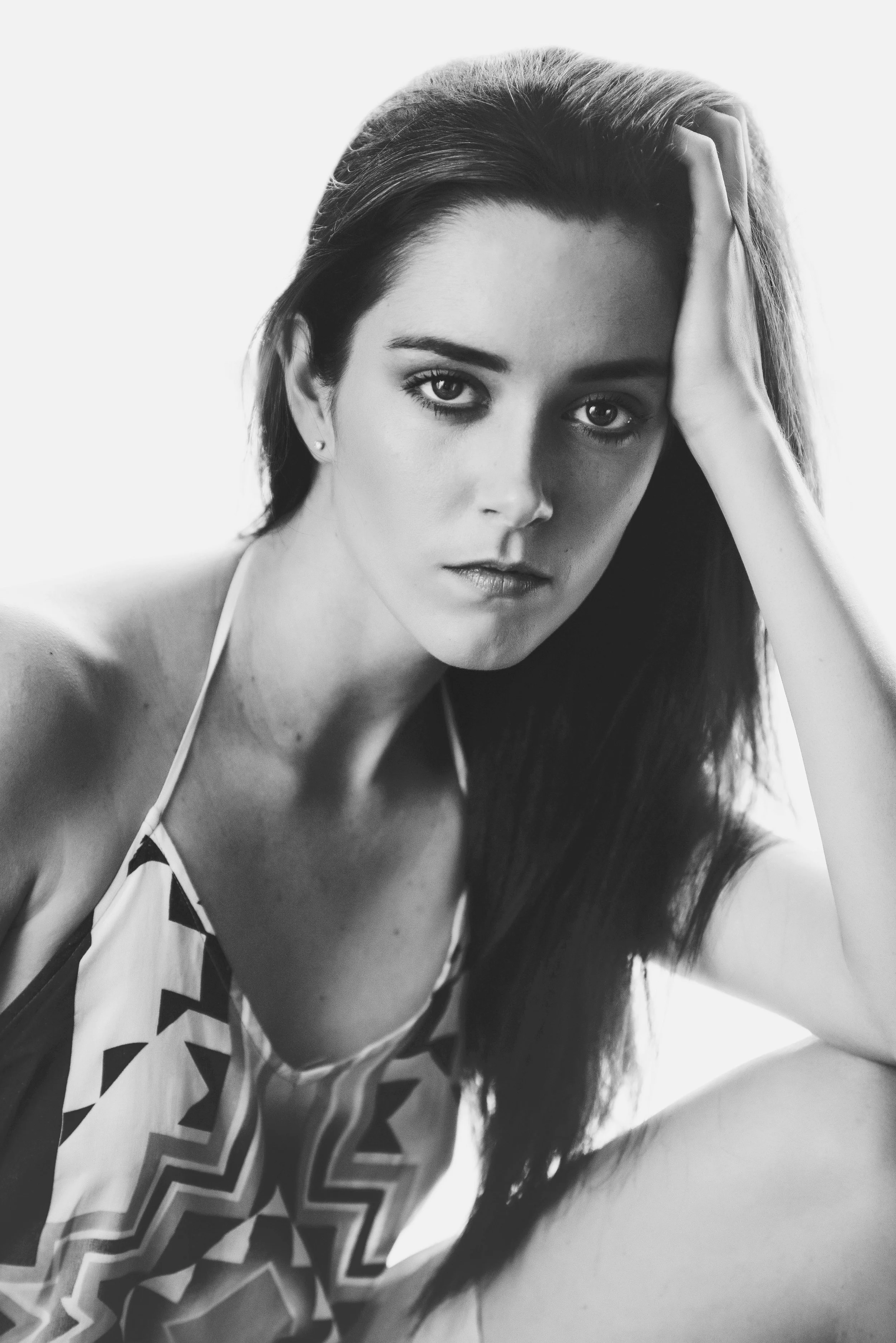 Black and white portrait of a woman with long hair, looking directly at the camera. She is resting her head on her hand, wearing a patterned top.