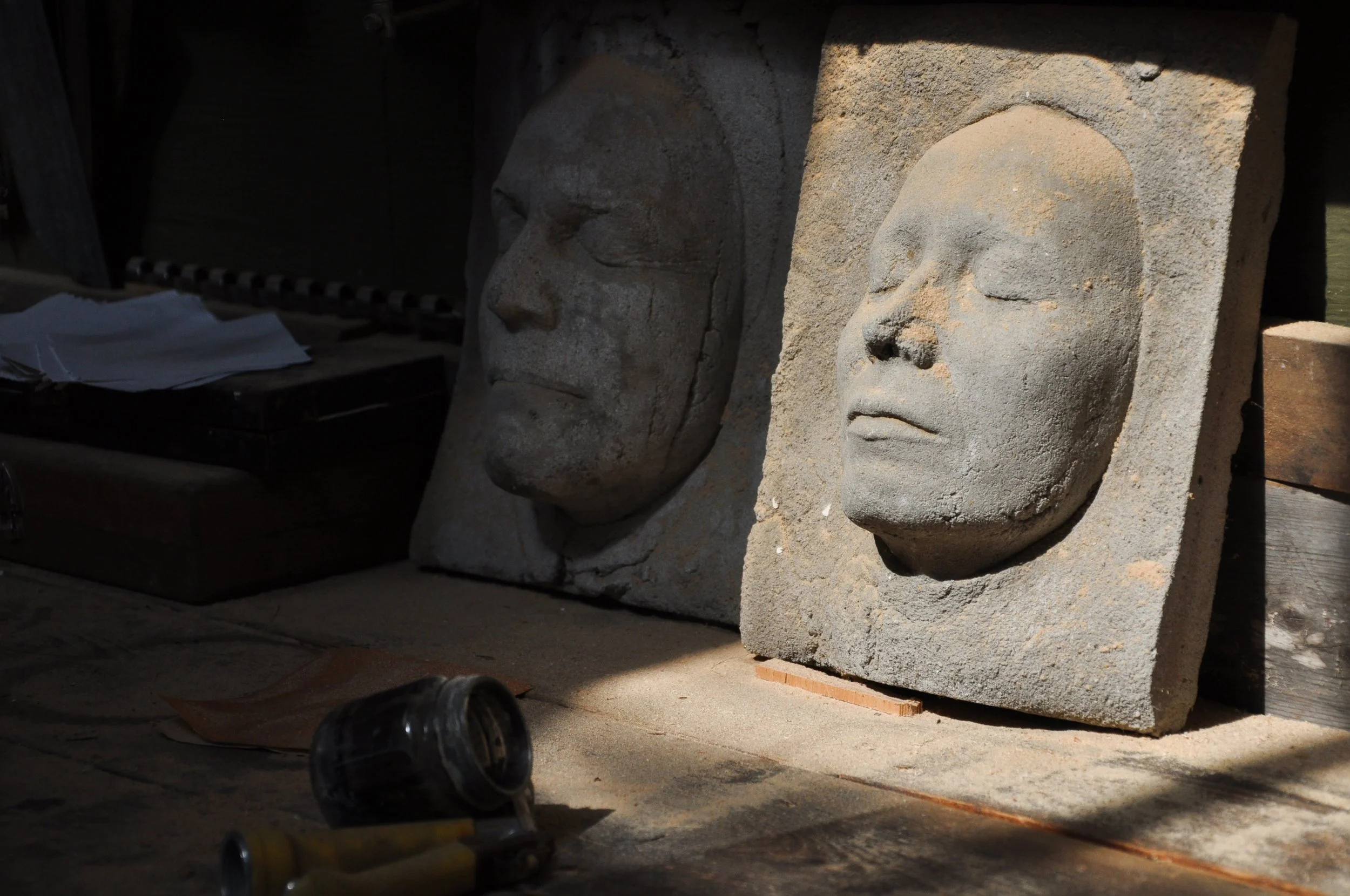 Two carved stone masks, one with closed eyes and both with calm expressions.