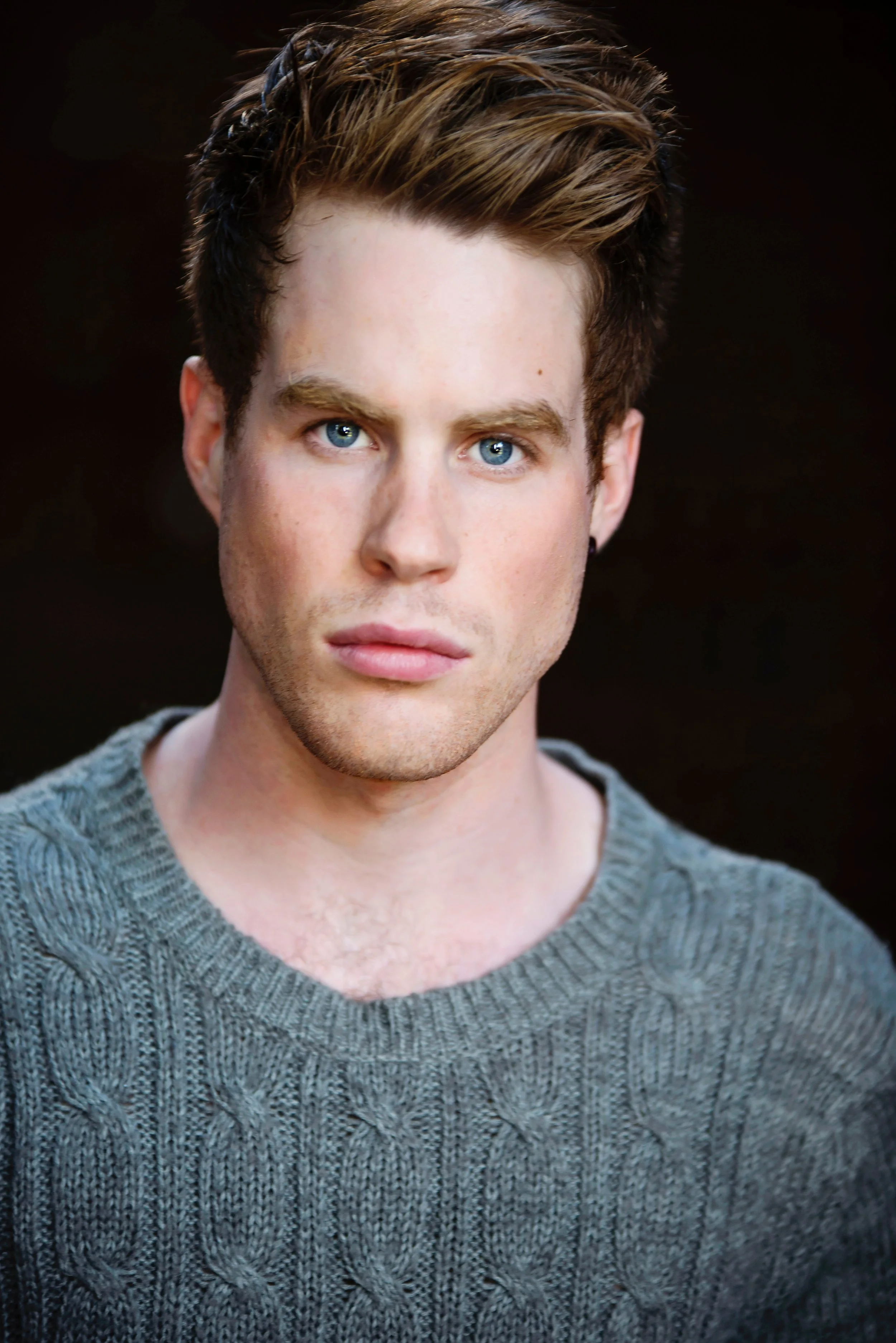 Close-up portrait of a young man with blue eyes and brown hair, wearing a gray knitted sweater.