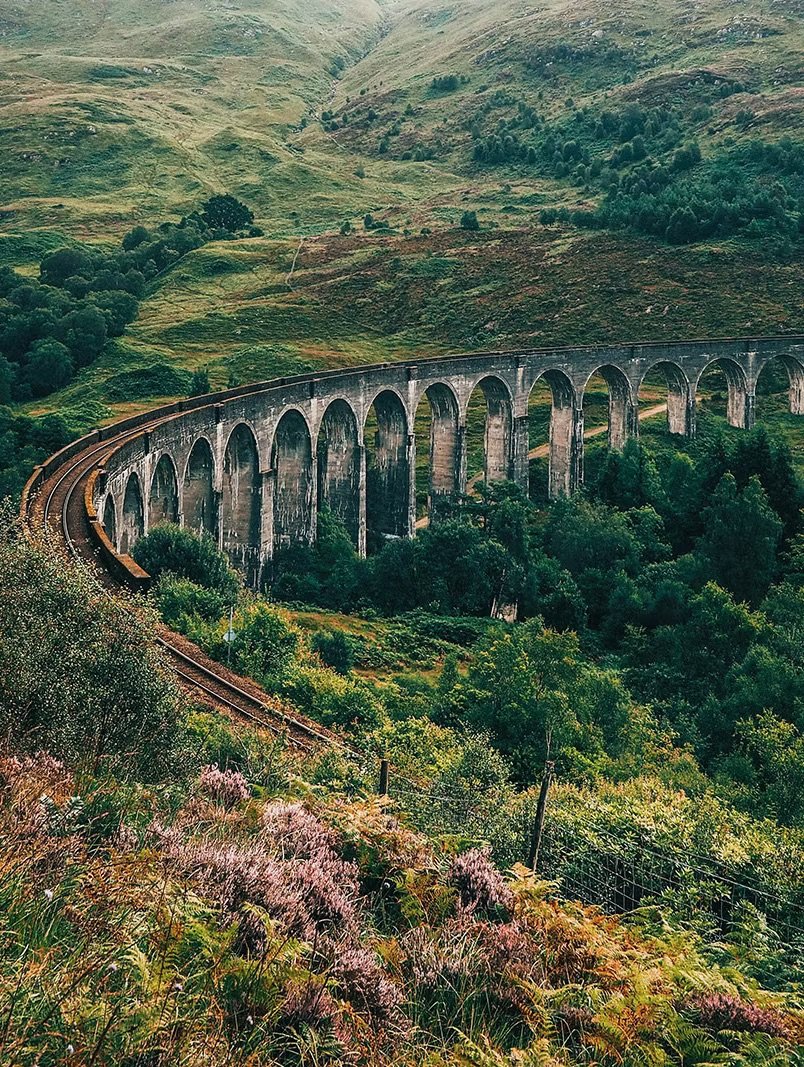 A scenic view of a curved railroad viaduct with arches stretching across a lush, green hillside.