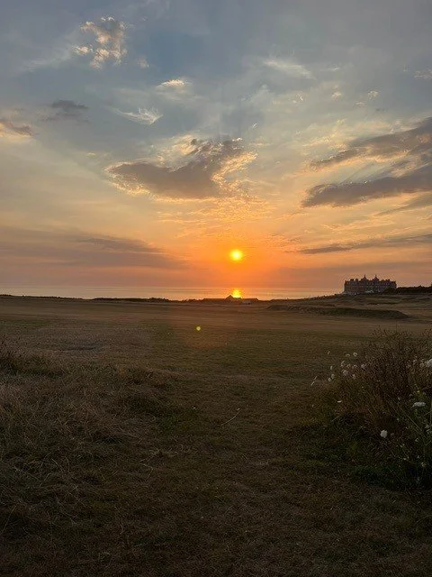 Sunset over a flat landscape with a distant castle on the right, with clouds and a mostly clear sky.