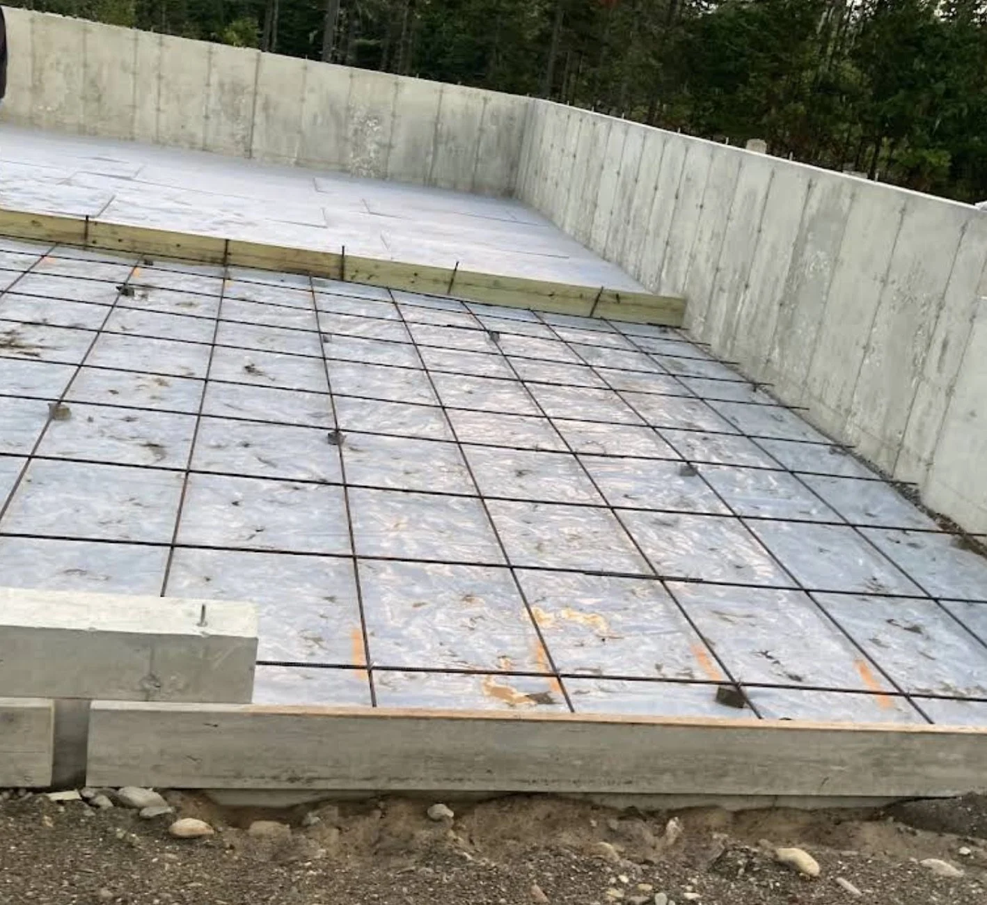 New Home Construction site with rebar grid in place on a concrete foundation. Wooden forms along the edges, concrete walls around the area, surrounded by trees in Marlton, New Jersey.