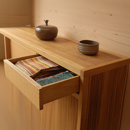 A wooden cabinet with an open drawer containing colorful fabric swatches, with two ceramic bowls and a small decorative jar on top.
