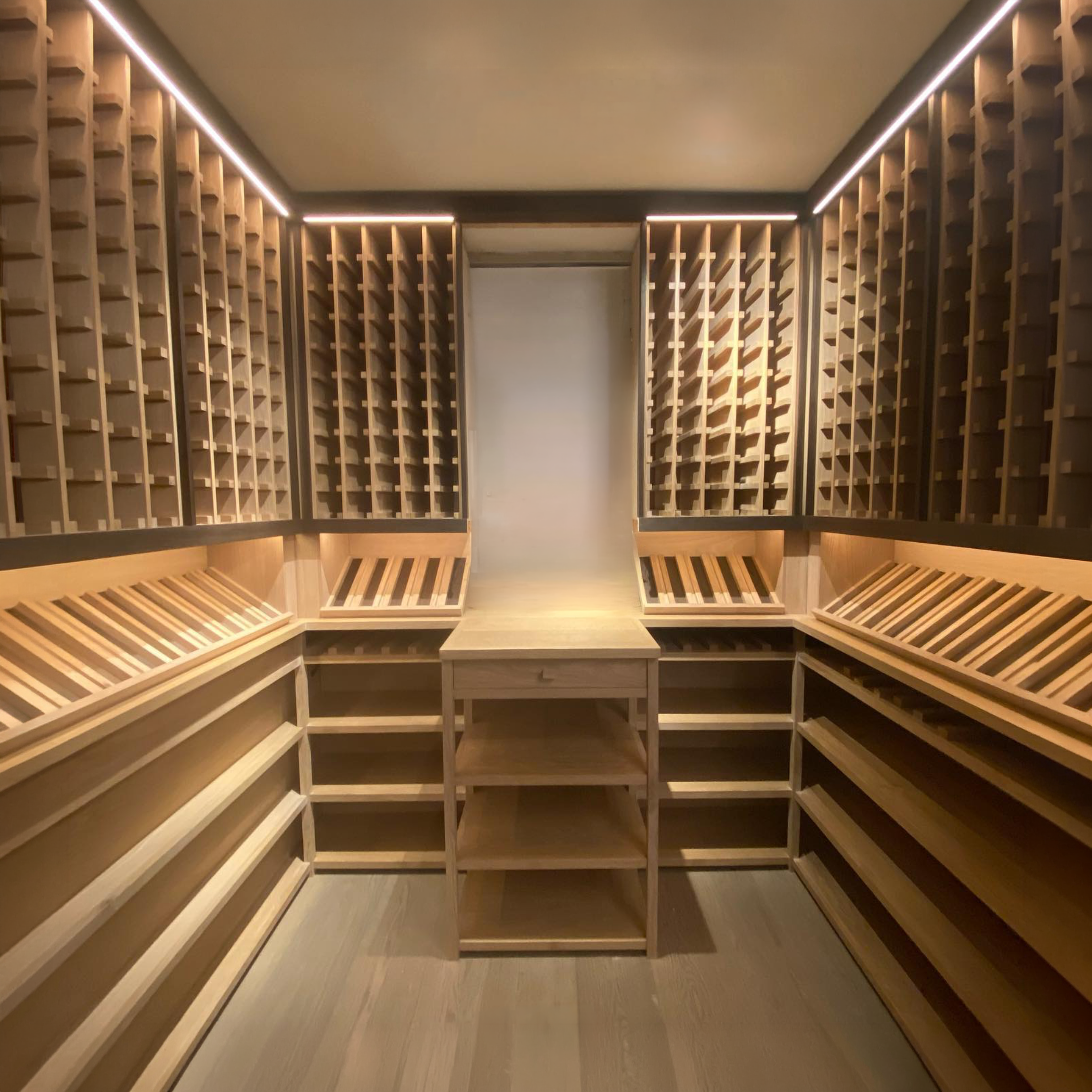 A room with wooden wine racks along the walls and benches in the center, illuminated by strip lighting on the ceiling.
