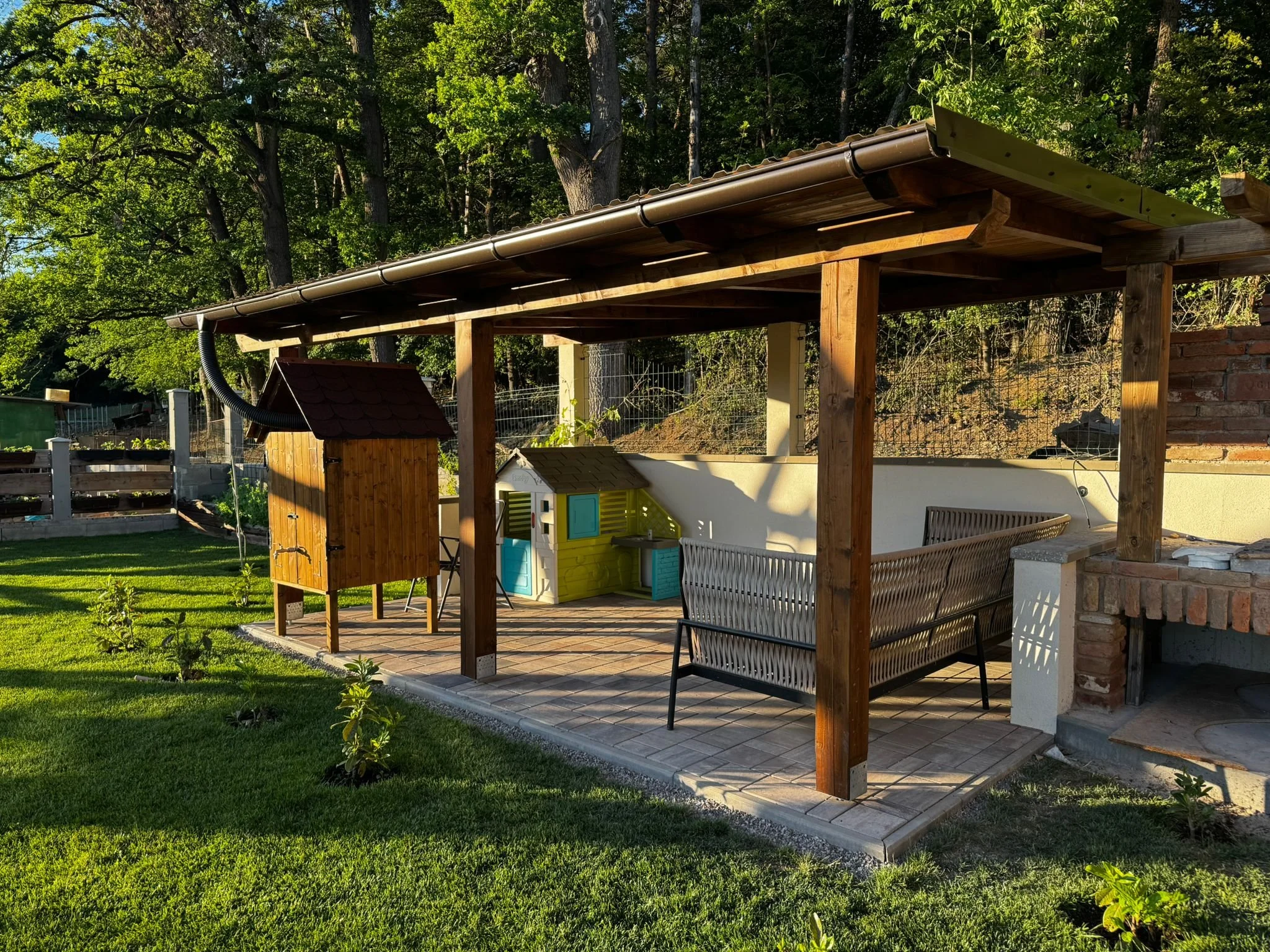 Wooden pergola installation with a brick pizza oven and an outdoor patio seating area. Realizace dřevěné pergoly s cihlovou pecí na pizzu a venkovním posezením na terase.