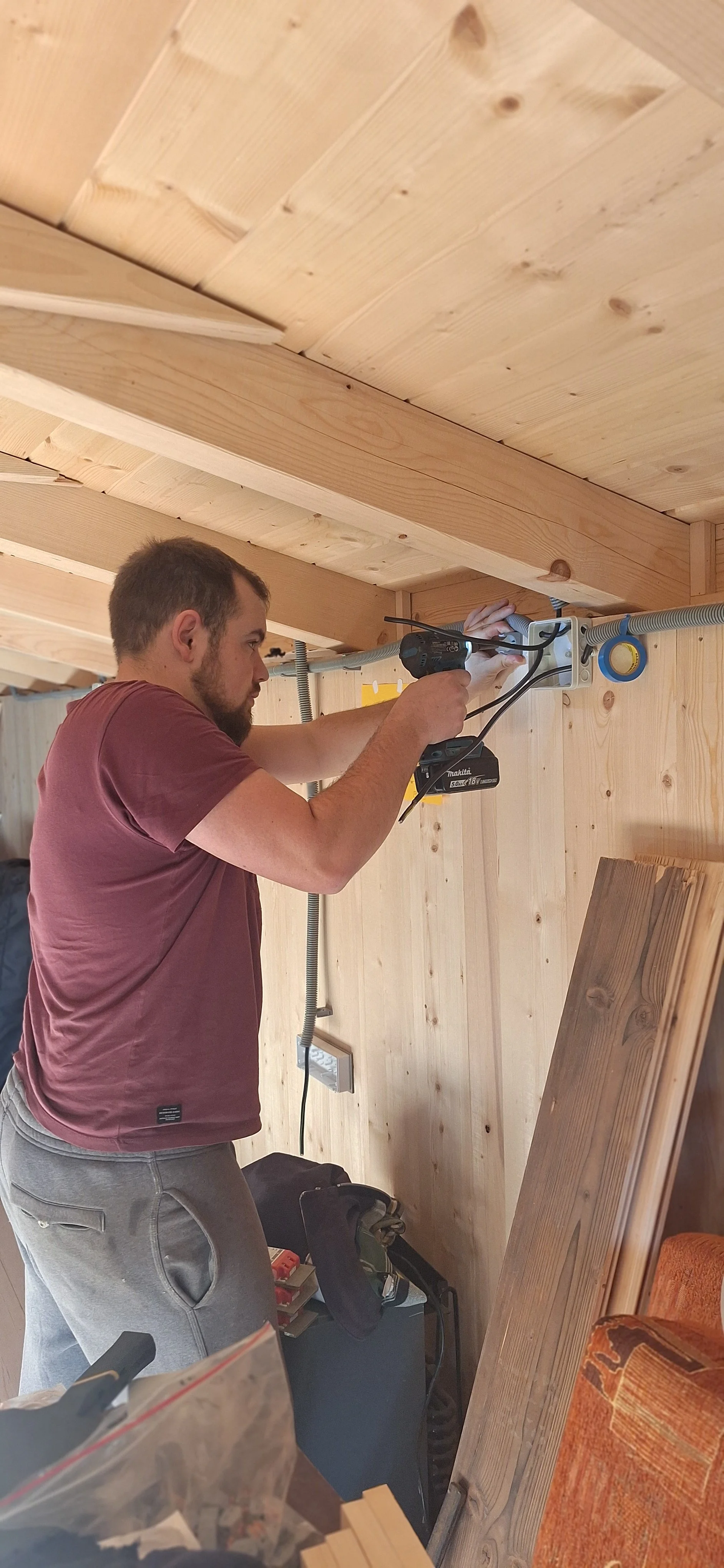 Man installing or working on electrical wiring inside a wooden room with wood-paneled walls and ceiling.