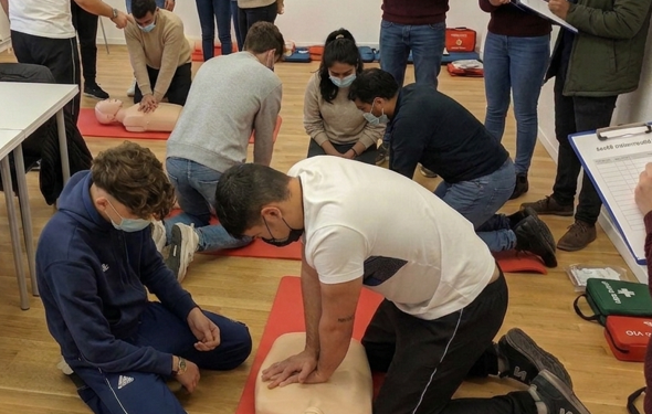 A group of people participating in a CPR training session, practicing on adult mannequins in a classroom setting.