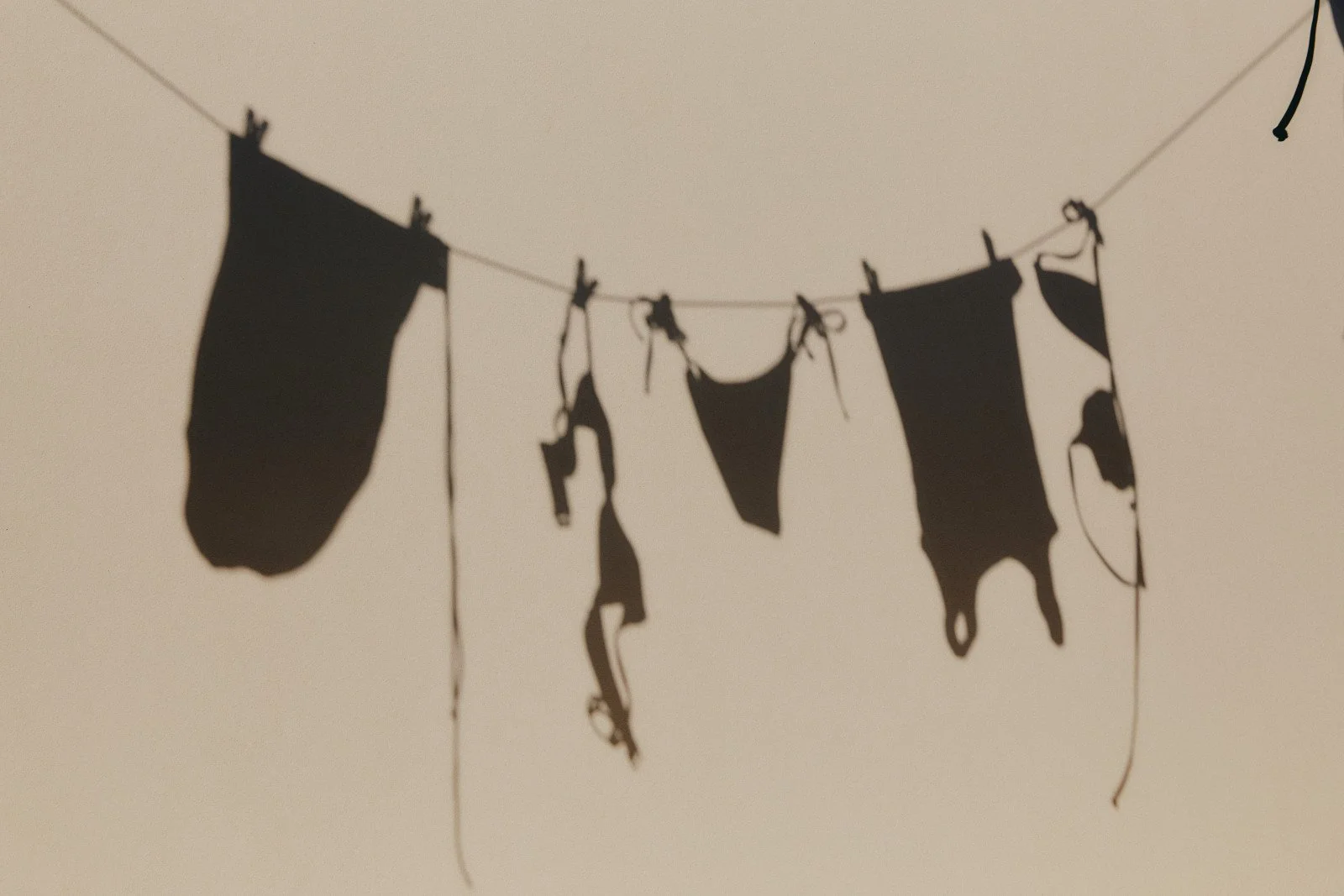 Black laundry hanging on a clothesline against a light background, casting shadows.