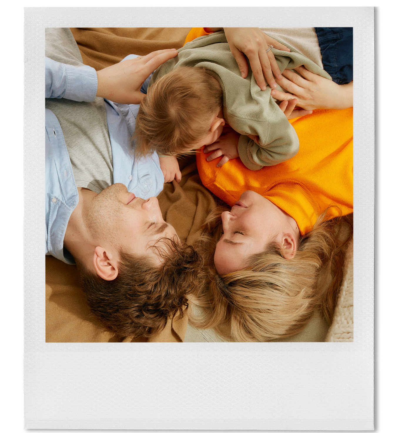 A family lying on the floor, with two adults and two children, face to face, with their noses touching and smiling.