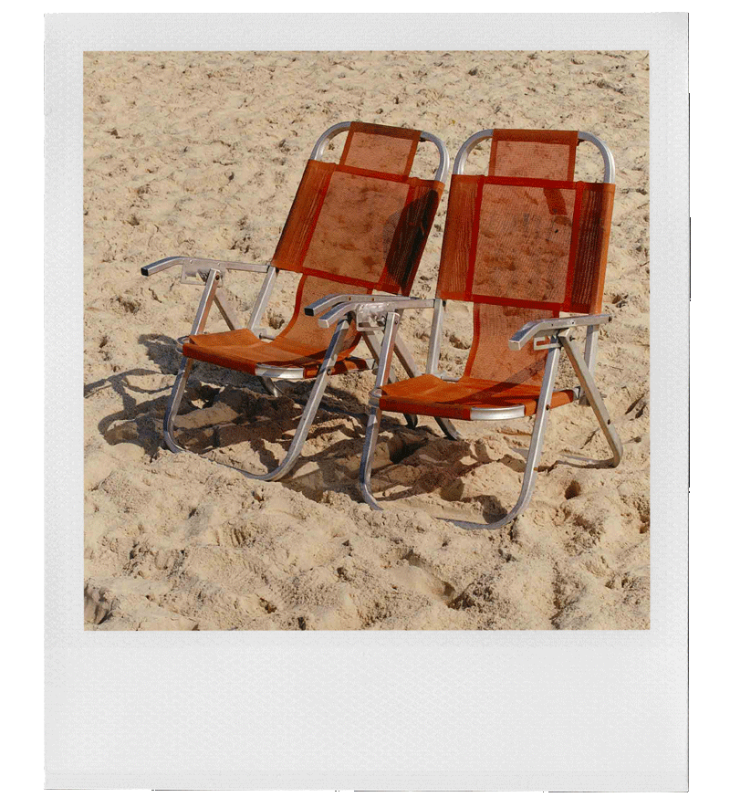 Two empty brown lounge chairs on a sandy beach, facing forward, with a slight shadow cast on the sand.