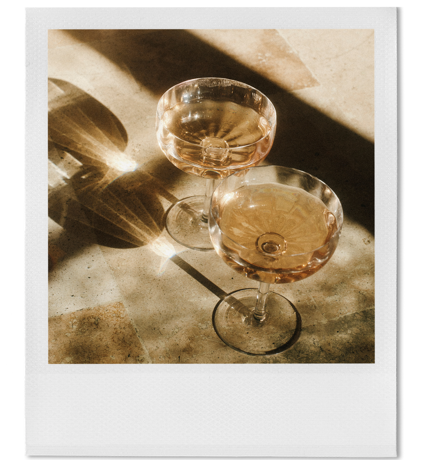 Two empty cocktail glasses with pinkish liquid, casting shadows on a beige tiled surface.
