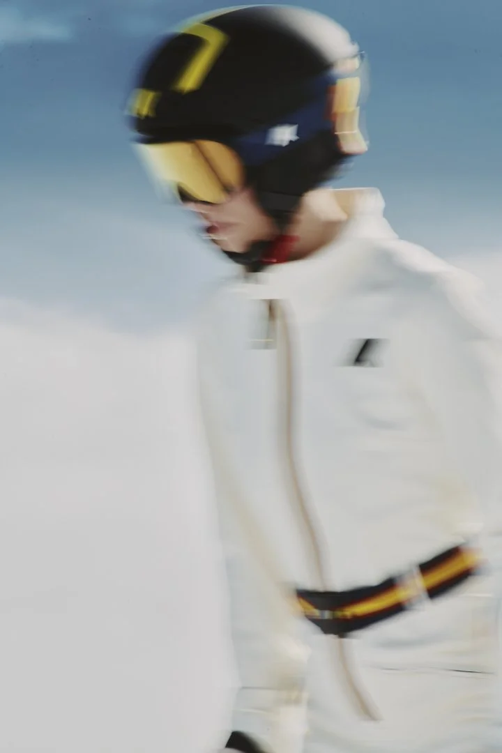Person wearing a black helmet with yellow accents and reflective goggles, dressed in a white jacket, in a snowy landscape.