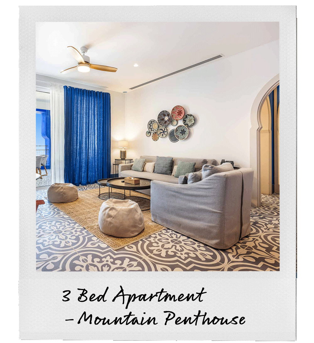 Living room with beige sofas, blue curtains, decorative wall art, patterned tile floor, bean bags, and a round coffee table.