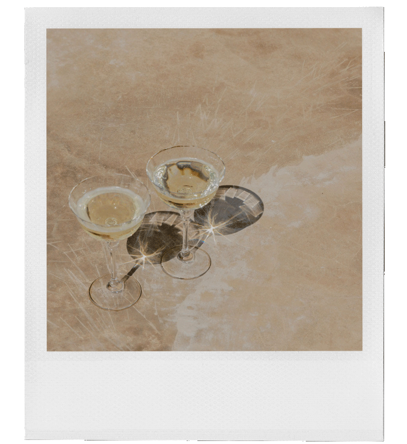 Two glasses of champagne on a beige marble surface, with reflections of light creating starburst effects in the glasses.