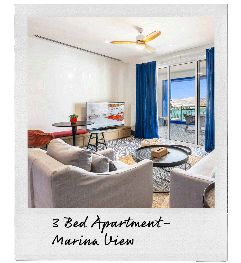 Living room with beige sofa, coffee table, TV, balcony with outdoor seating, blue curtains, ceiling fan, and mountain view