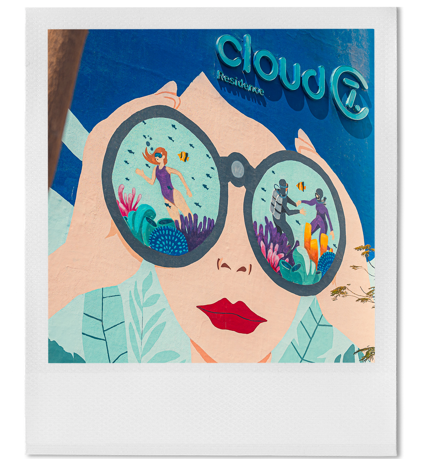 A mural of a woman wearing sunglasses with an underwater scene reflected in the lenses, featuring divers, fish, and coral reefs.