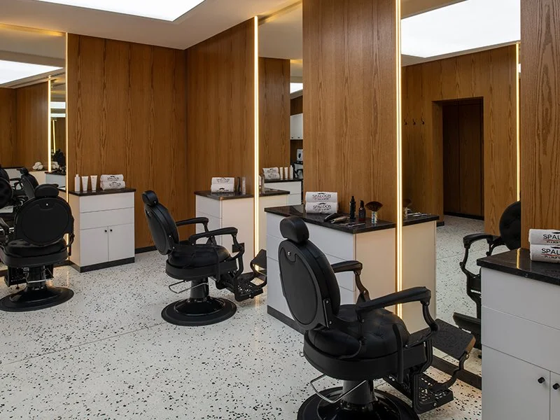 Interior of a modern barber shop with black barber chairs, white cabinets, and wooden wall panels.