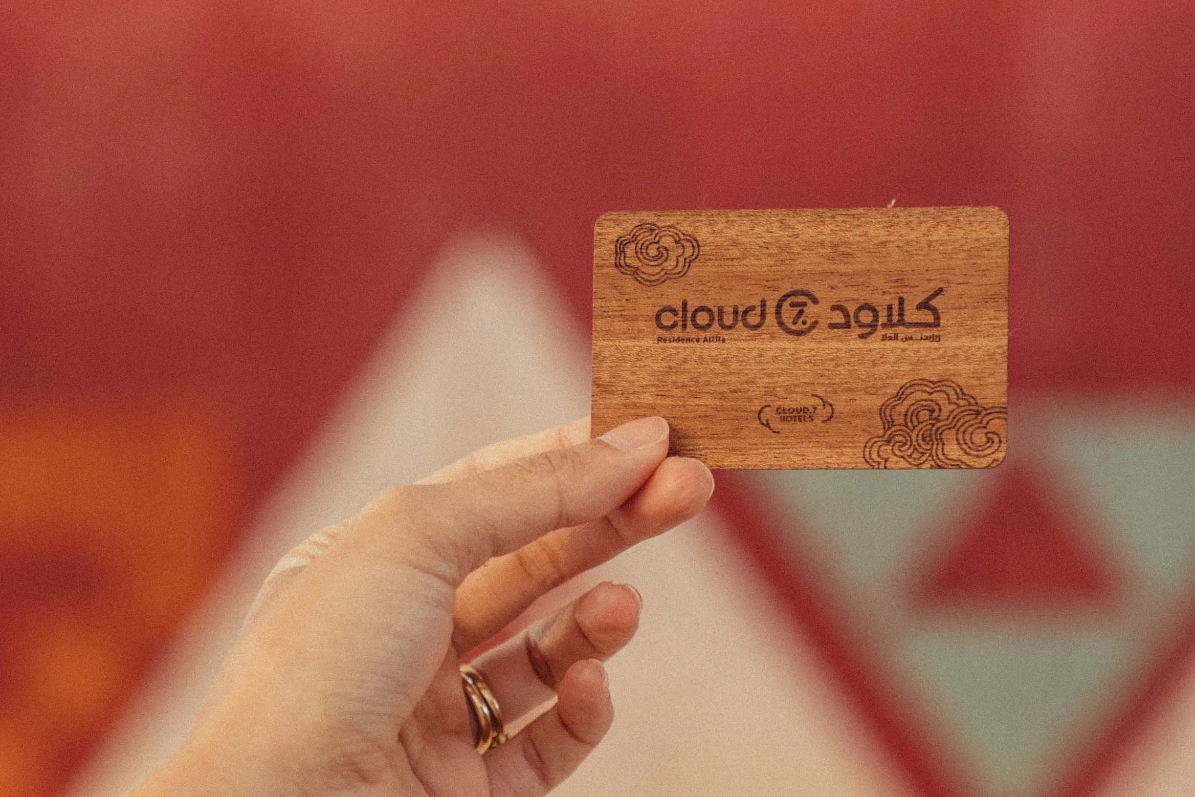 A person's hand holding a wooden card with the brand name 'cloud T' and a cloud logo, with the words 'Residence Allah' and some decorative cloud illustrations.