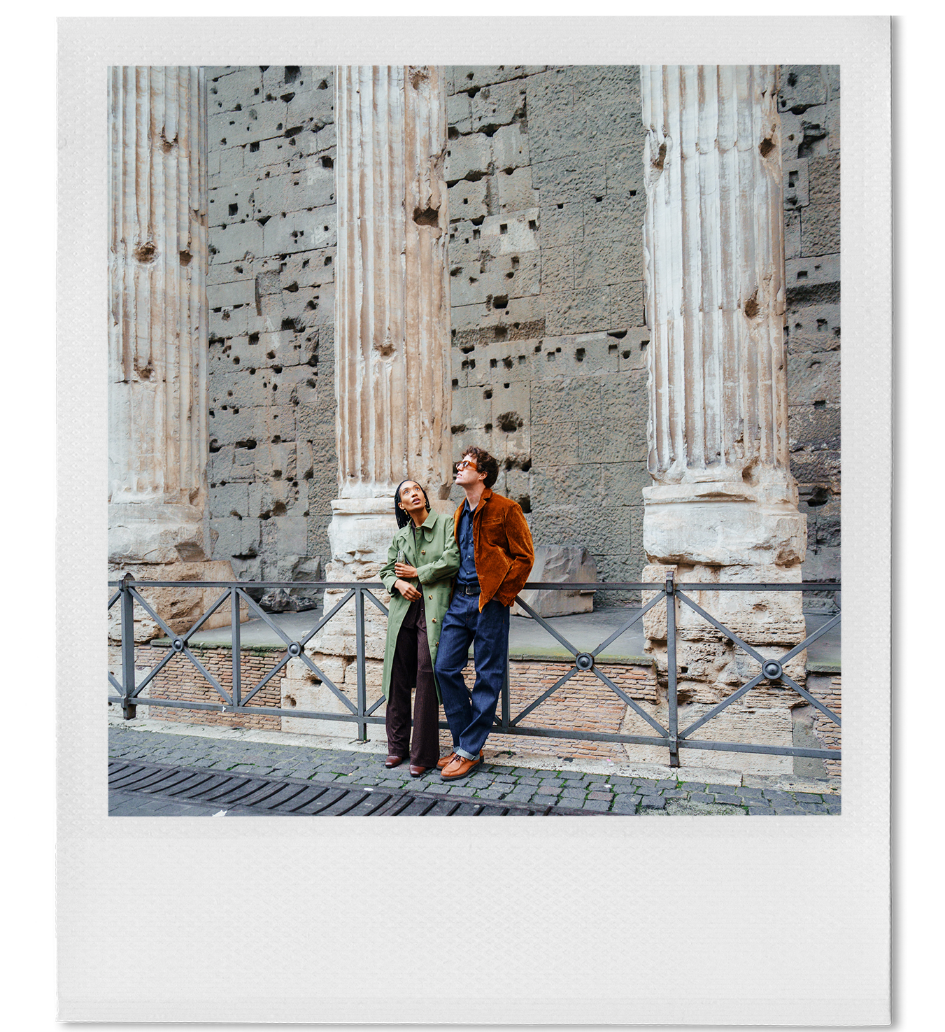 Two people standing in front of ancient ruins with large stone columns, gazing upward.