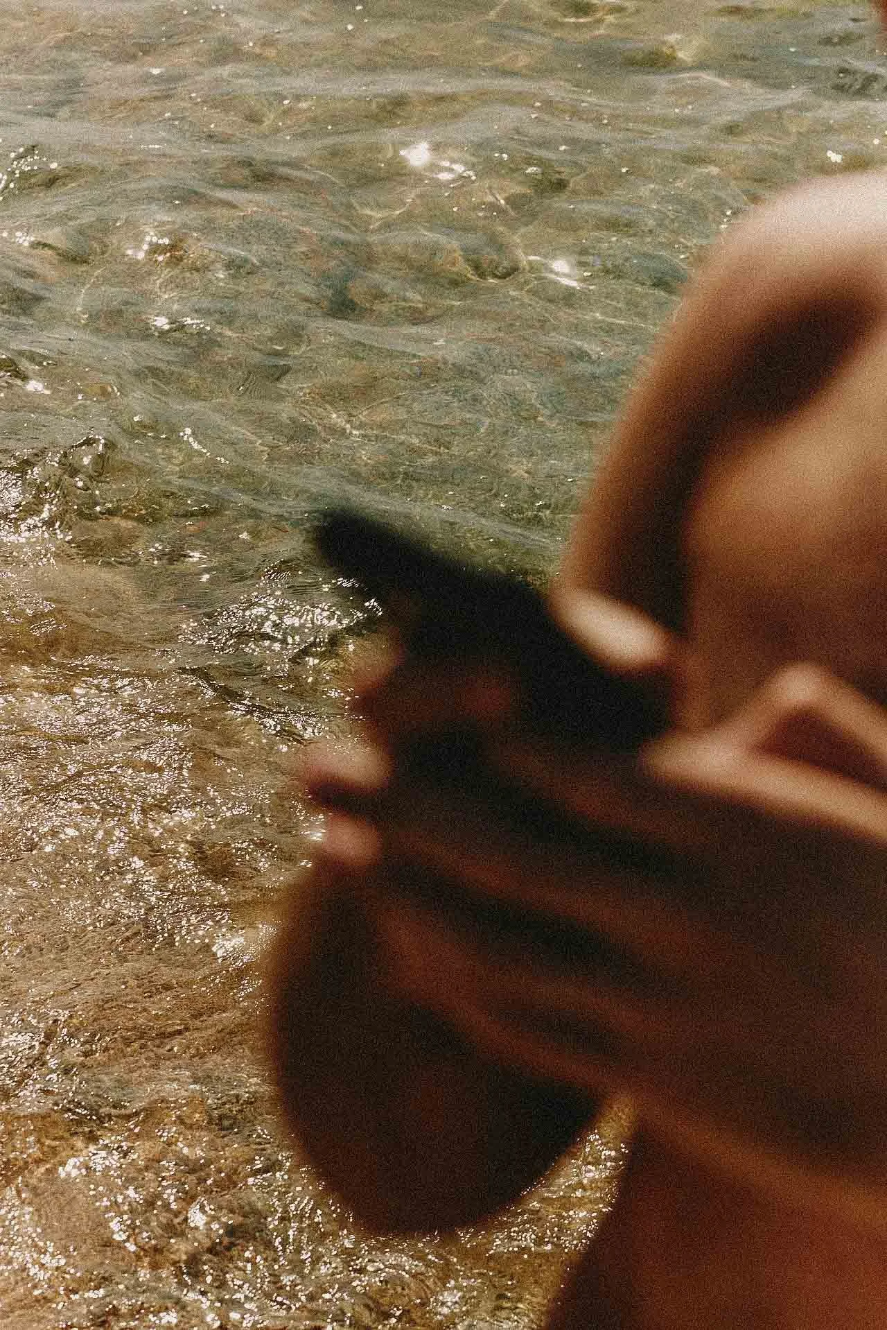 Blurred person in the water at the beach, with visible waves and sand.