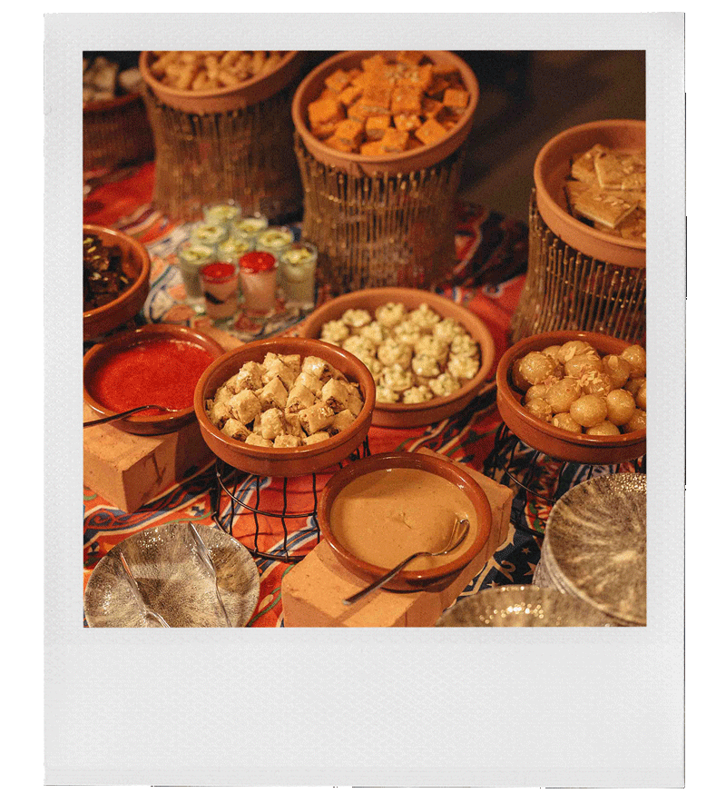 Assorted bowls of dips, cheeses, and snacks on a colorful tablecloth, including tortilla chips, popcorn, and various sauces.