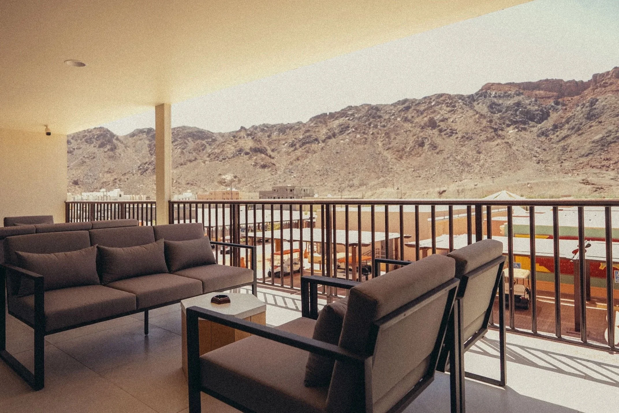 Outdoor patio area with brown sofas and tables, overlooking a mountainous landscape in the background.