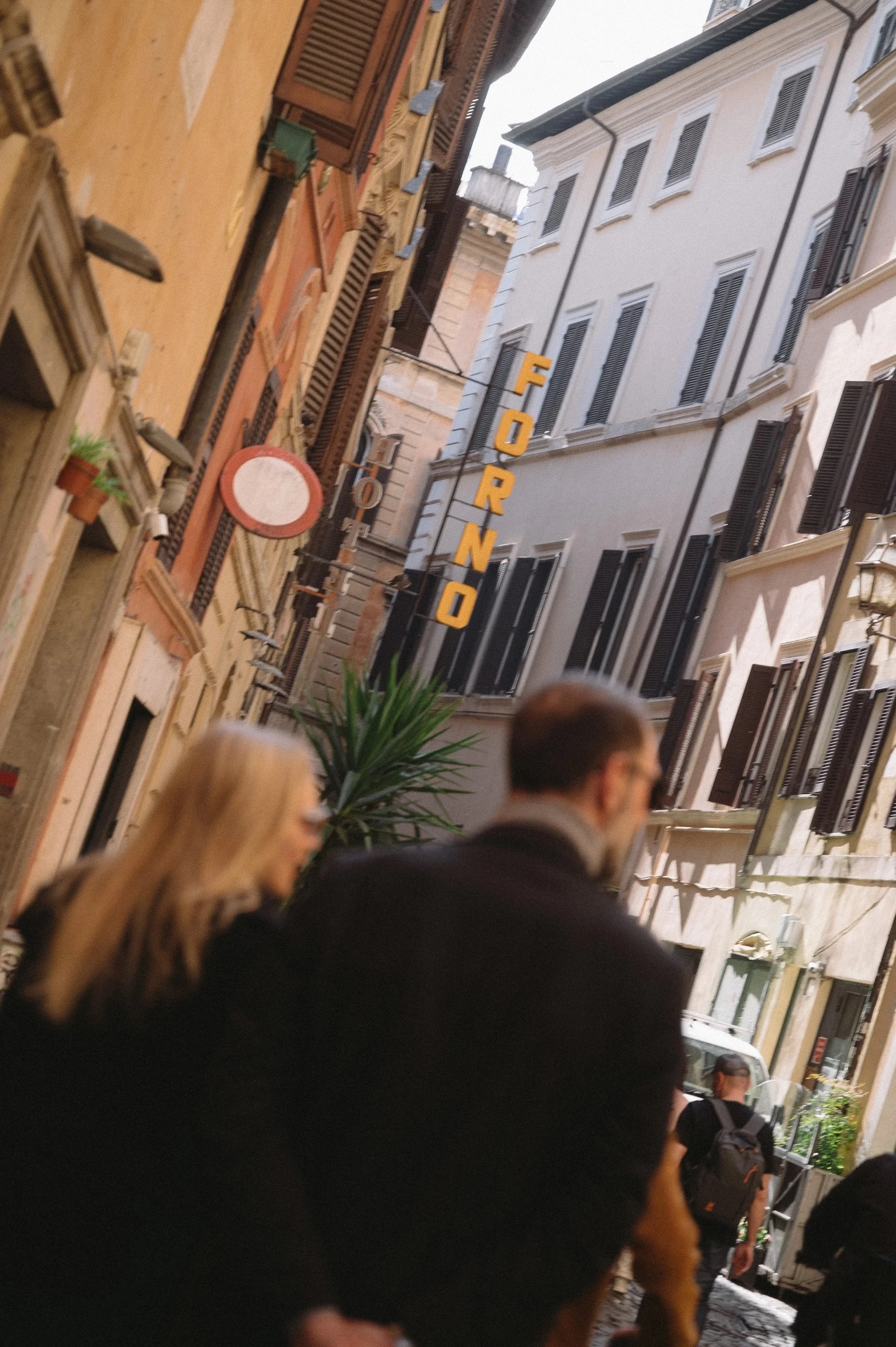 People walking on a street with buildings and a sign that reads 'FORNO' in the background.