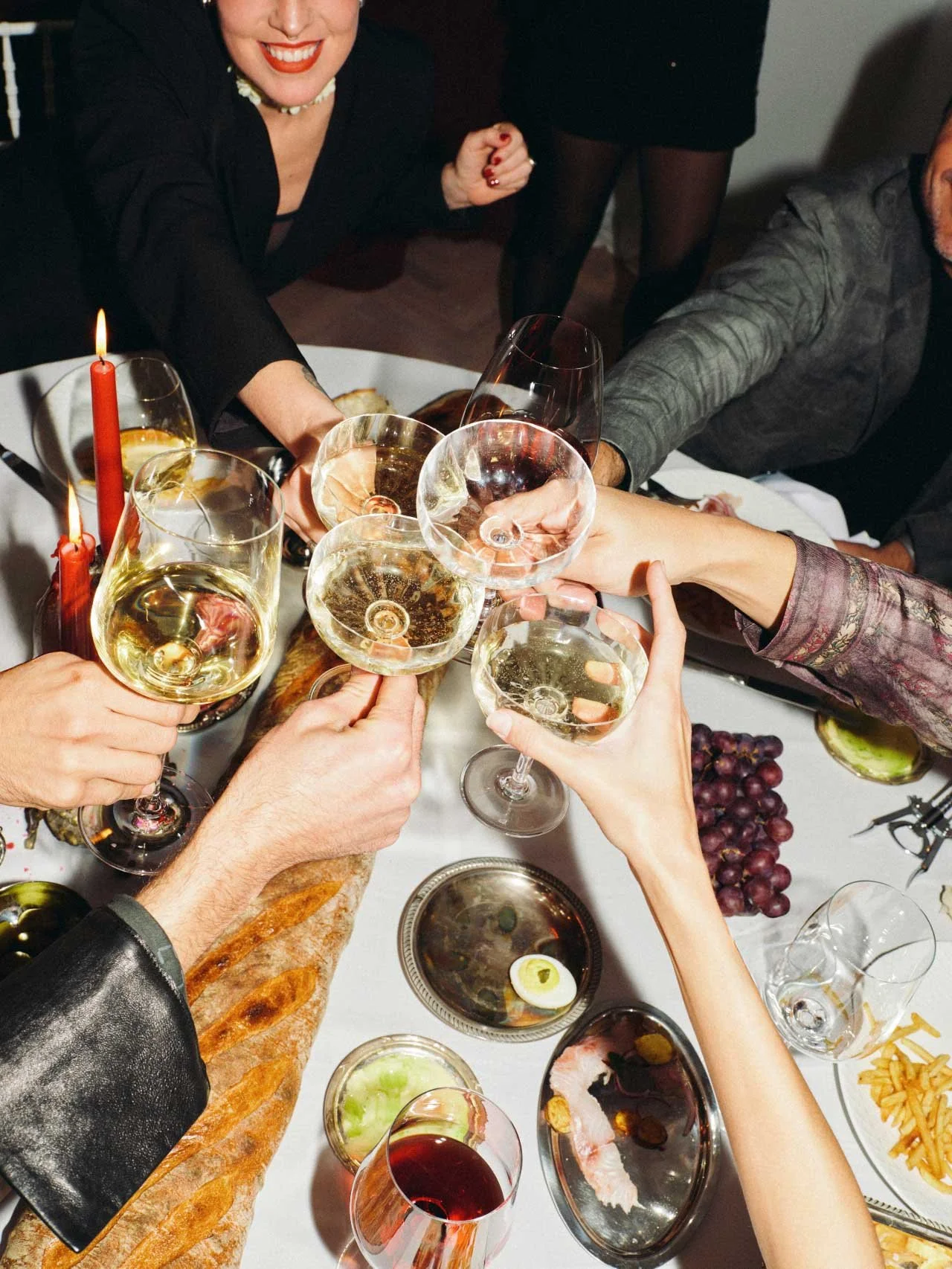 People raising glasses of white wine in a toast at a dinner party.