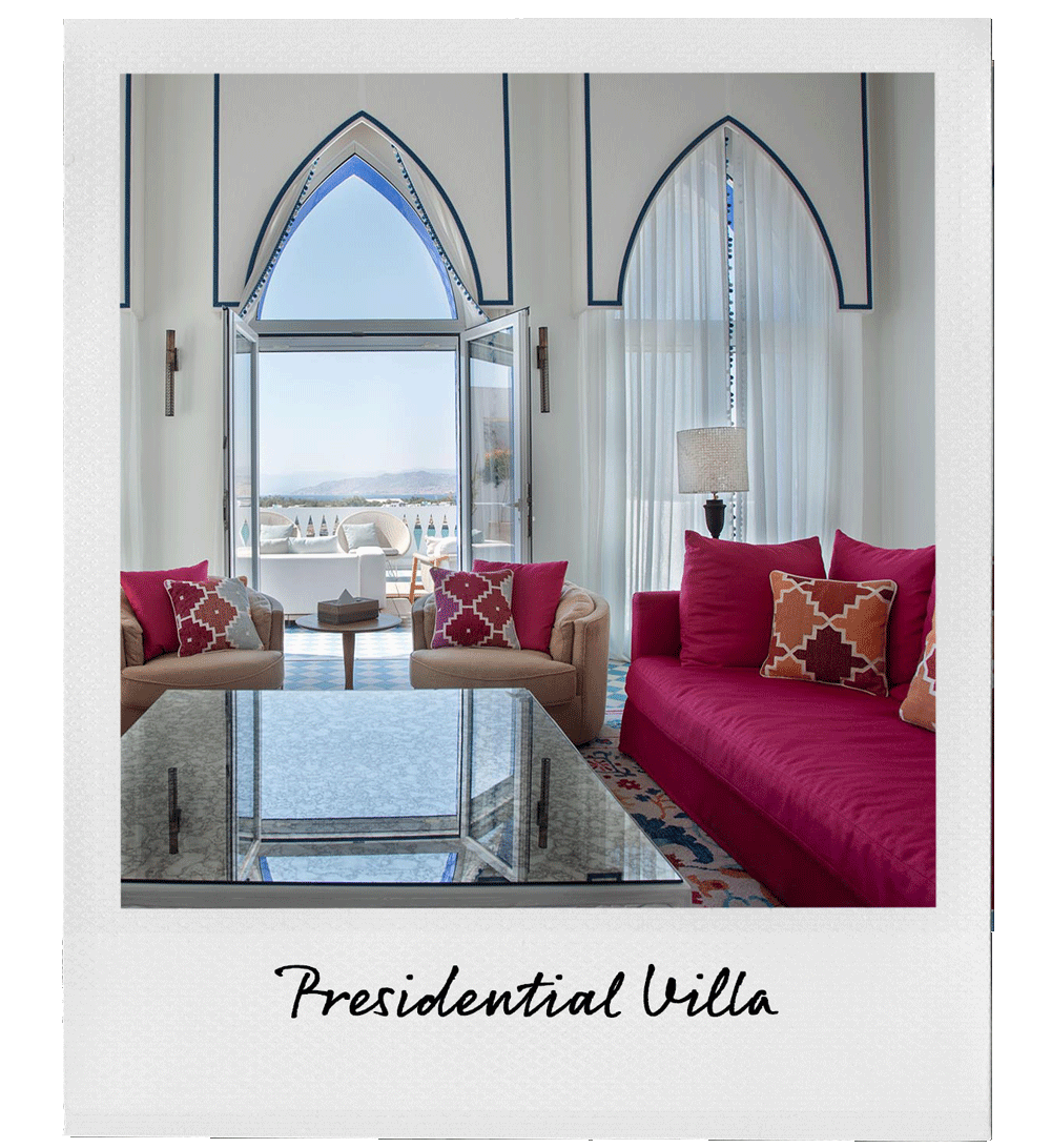 The living room features a large window and balcony door with arched design, revealing a scenic outdoor view. Inside, there are red and beige sofas with patterned pillows, a glass coffee table, and white curtains. A lamp and decorative elements add to the room's elegant, airy atmosphere, labeled 'Presidential Villa' beneath the image.