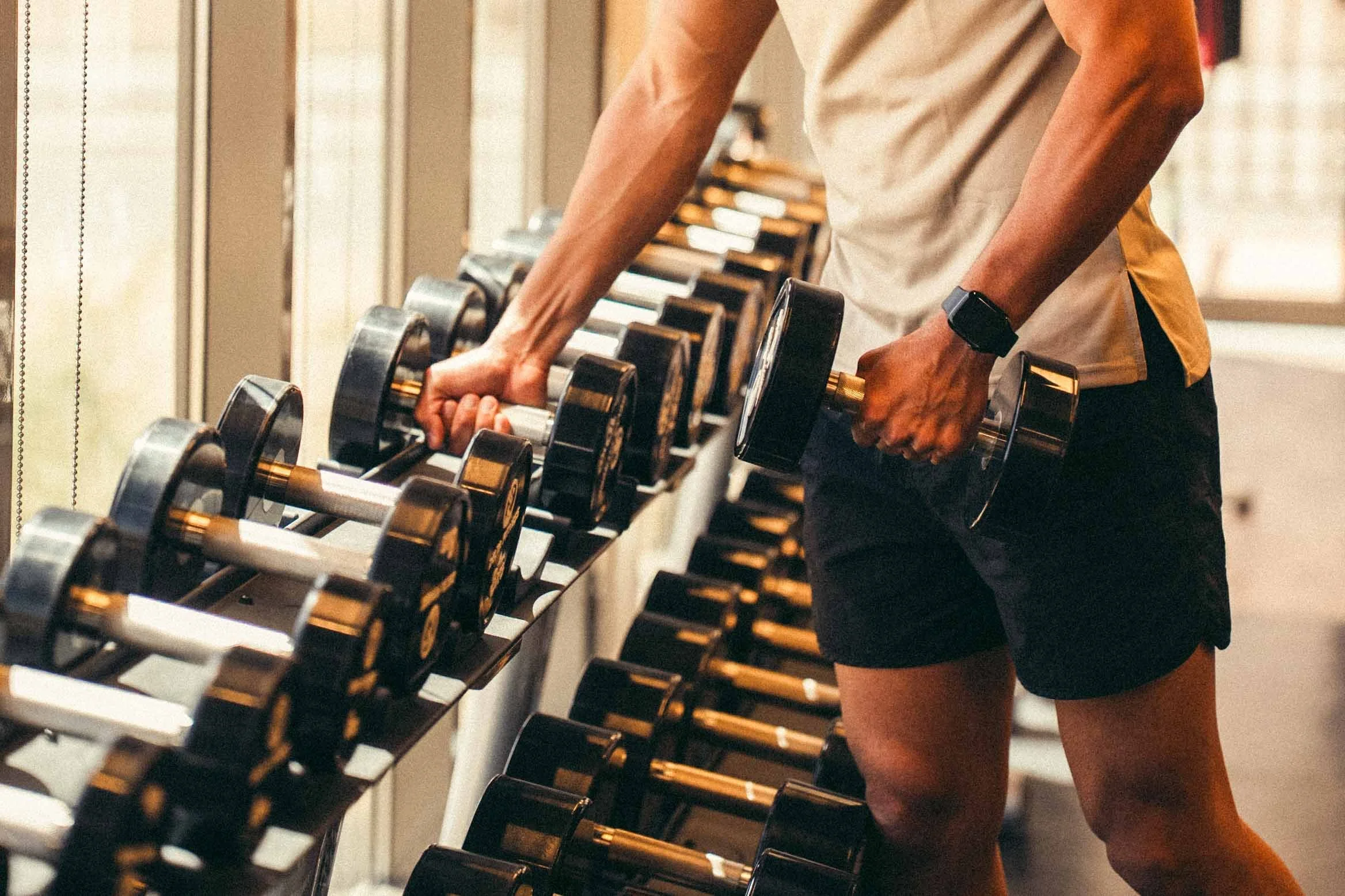 Person lifting dumbbells in a gym, wearing a smartwatch and athletic attire.