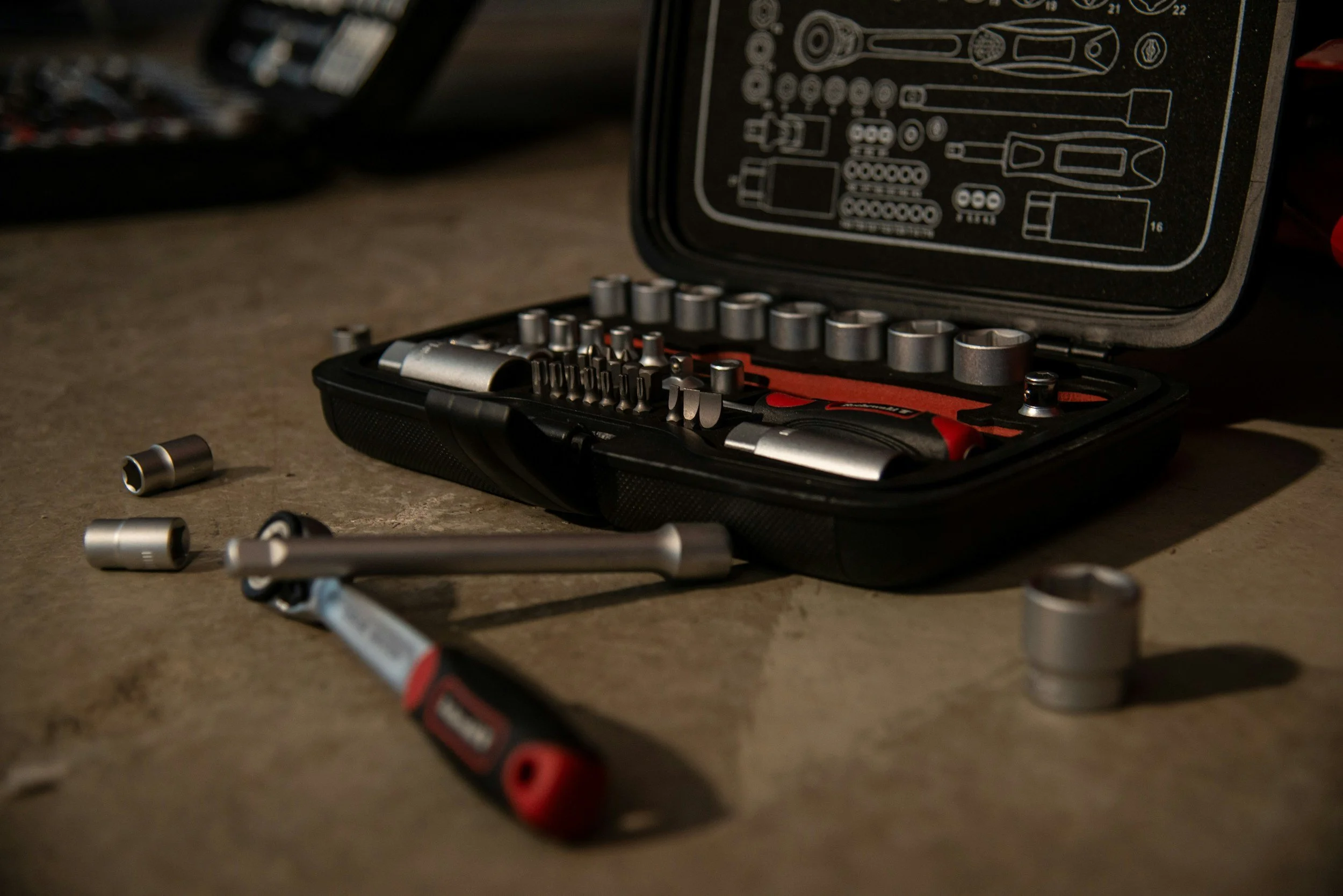 A partially open toolbox with various sockets and tools inside, resting on a work surface. Some tools are also scattered around the toolbox.