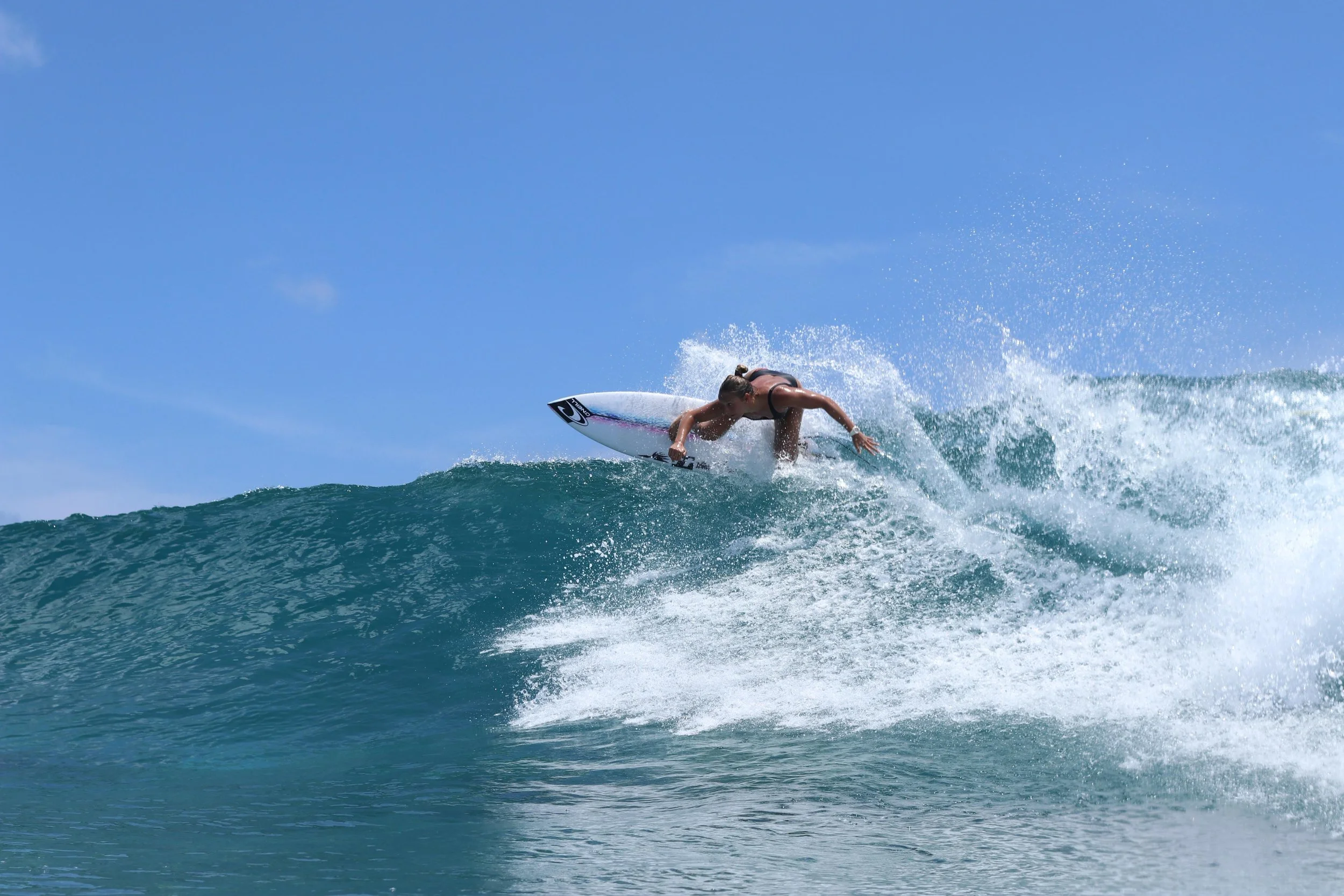 Una surfista donna, Valentina Vitale, che sta scendendo una cresta di onda in mare durante una giornata di sole.
