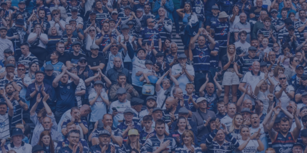 A large crowd of sports fans wearing blue and white, some clapping and cheering at a sports event.