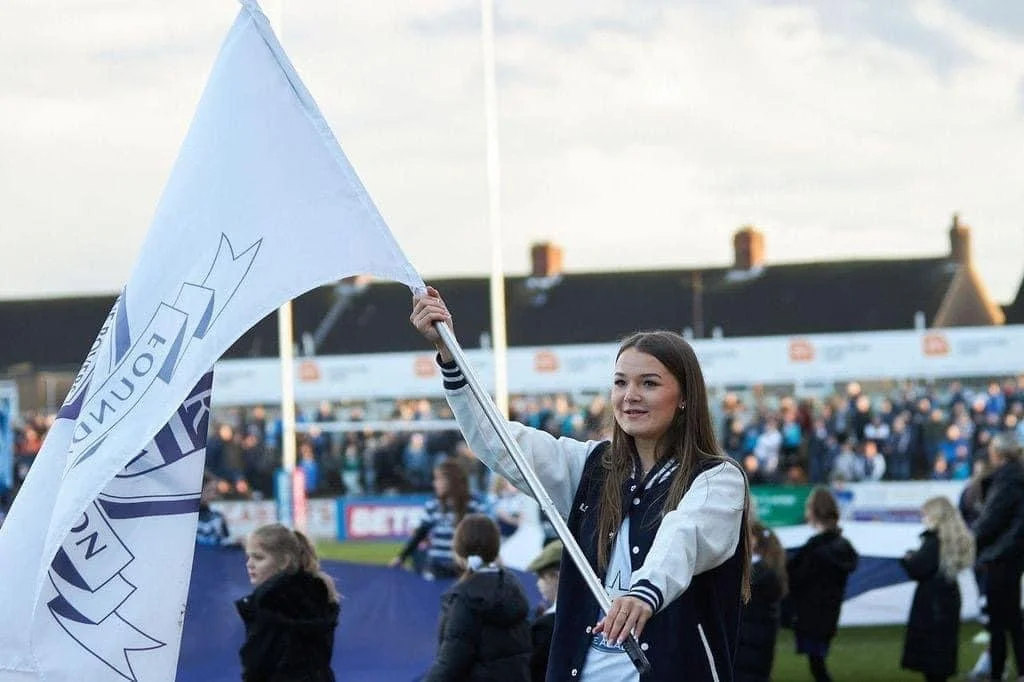 A woman holding a flag at a sports event with a crowd of spectators in the background.