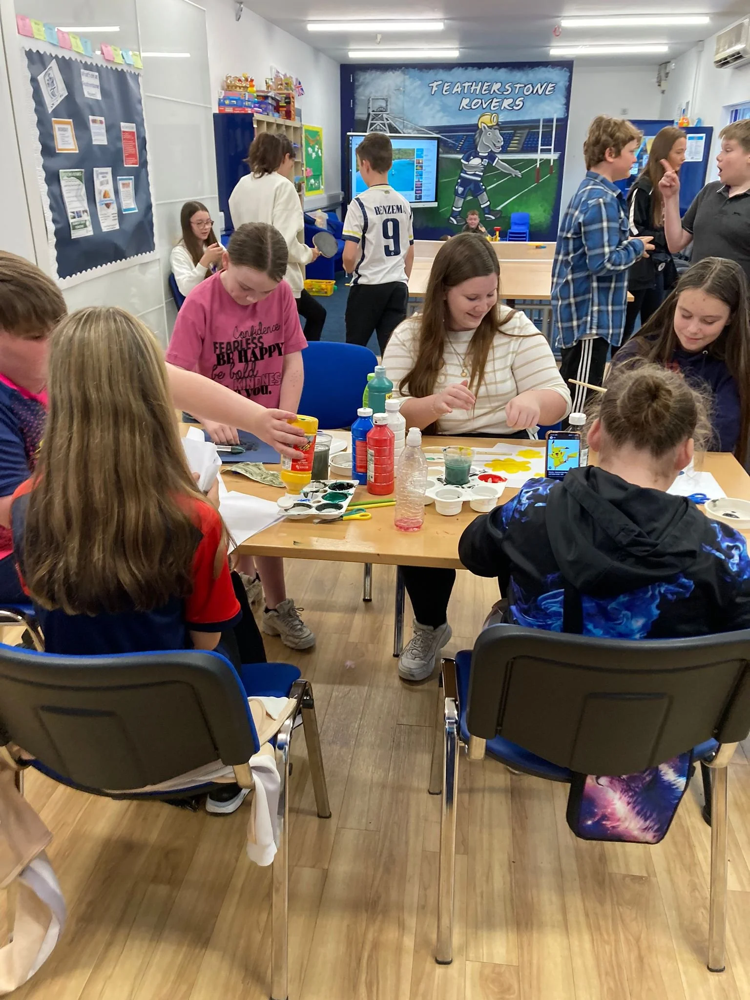 Children engaging in arts and crafts activity in a classroom with colorful supplies and a mural of a horse jockey on the back wall.