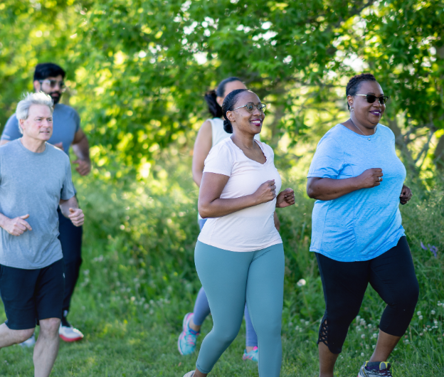 Group of diverse people jogging outdoors on a sunny day with green trees in the background.