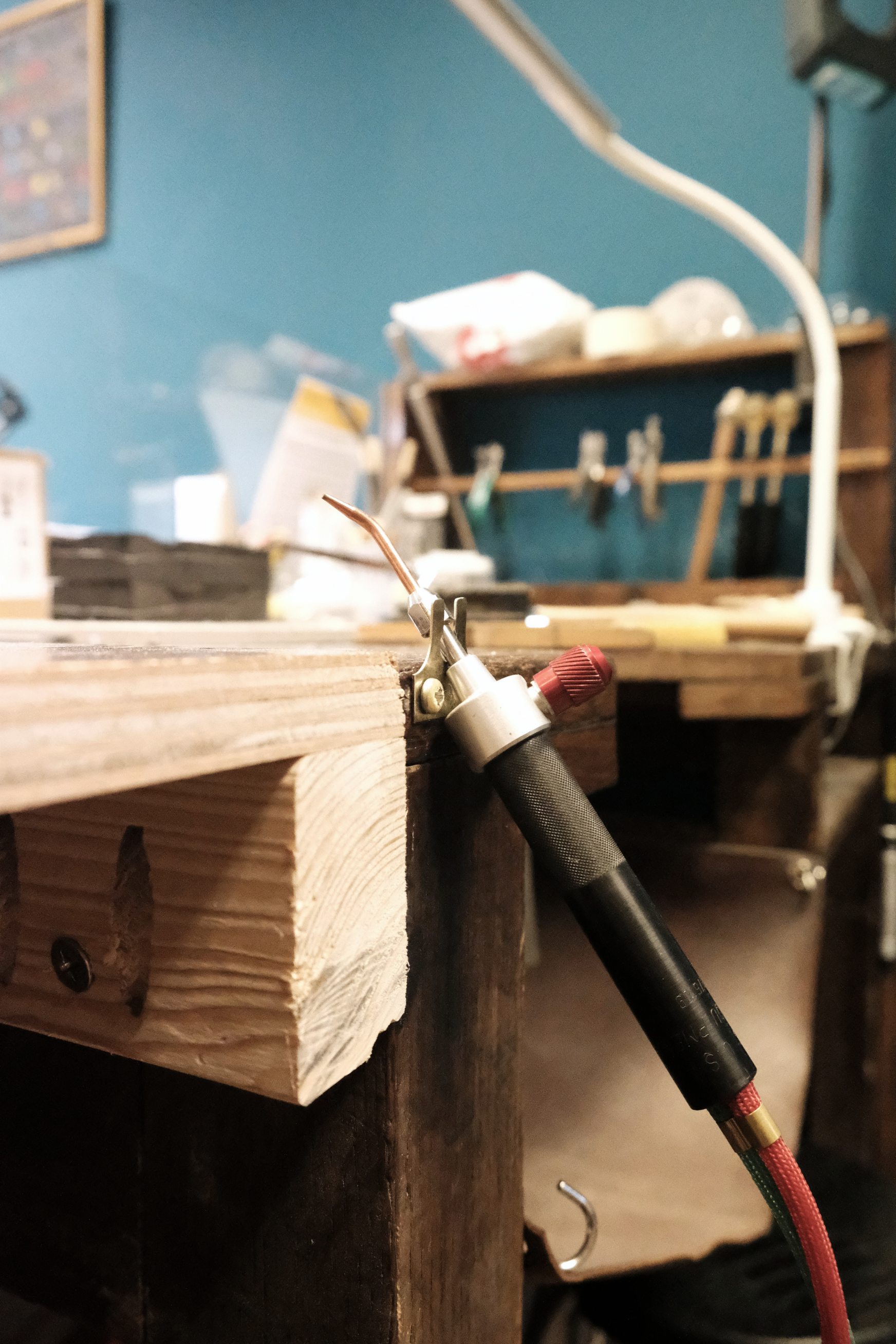 Close-up of a soldering iron touching a wooden block in a workshop setting, with tools and materials in the background.