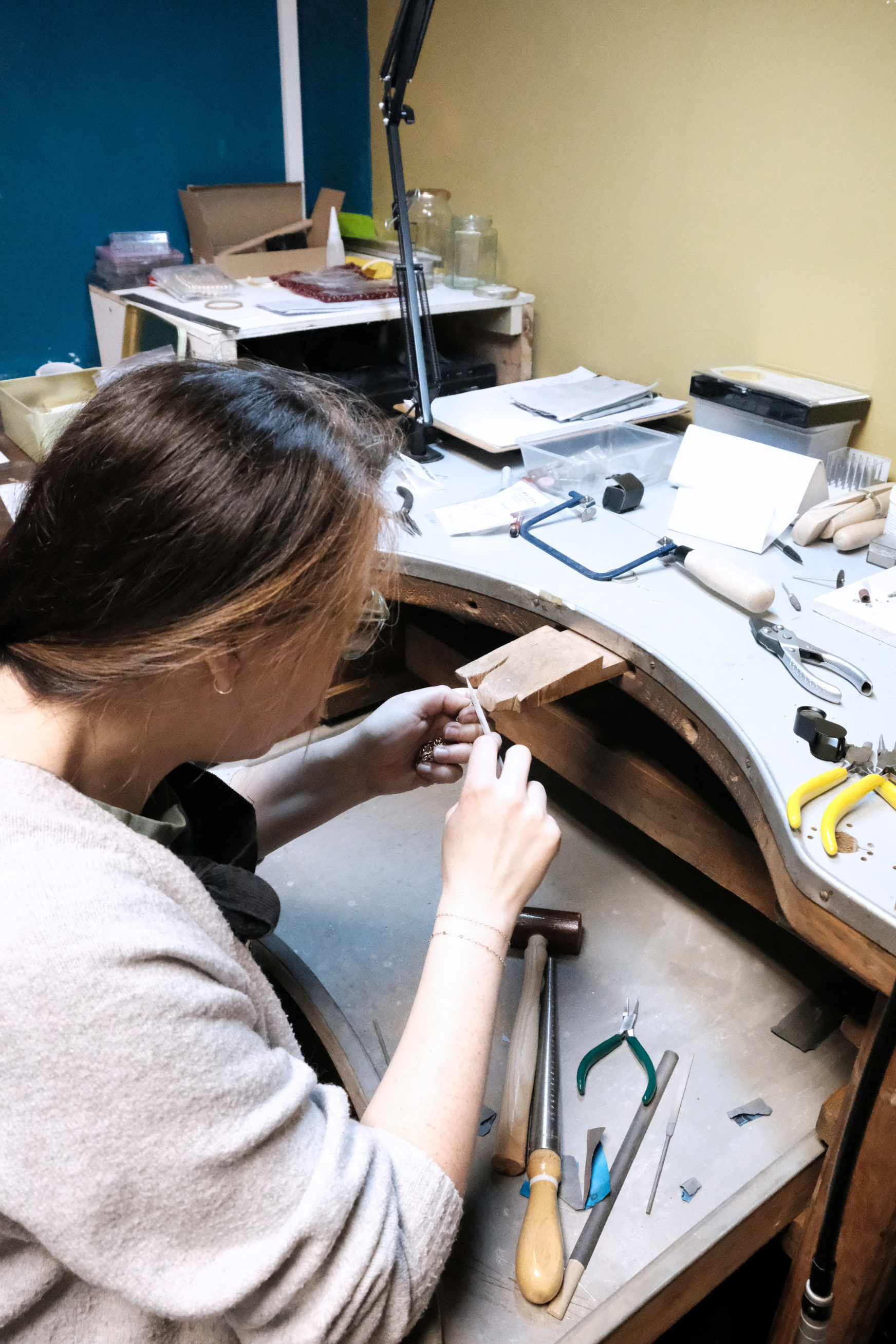 A goldsmith working on a craft project at a cluttered workbench with various tools and materials.