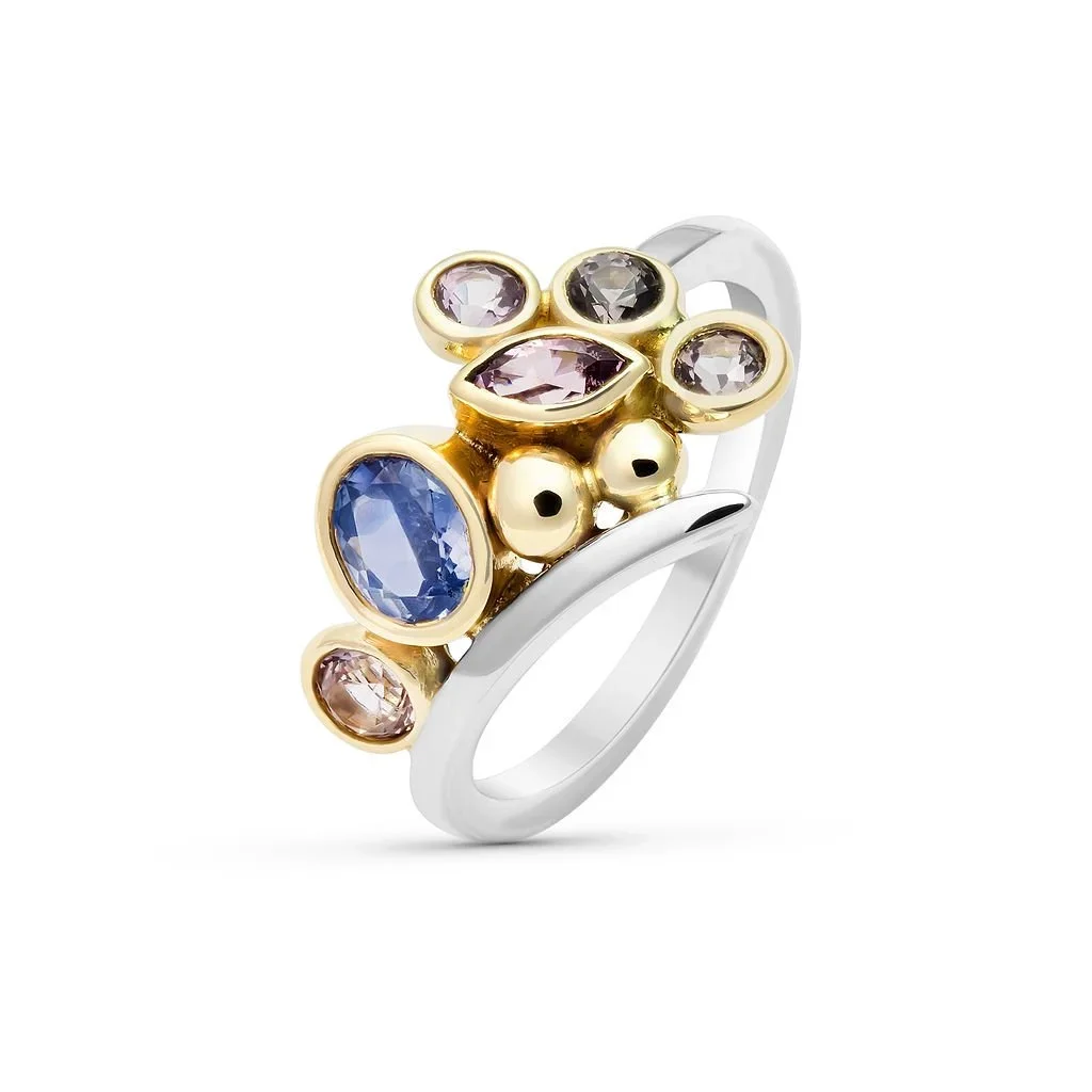 A multicolored gemstone ring with a gold and silver band, featuring various oval and round cut stones in purple, blue, gray, and pink.