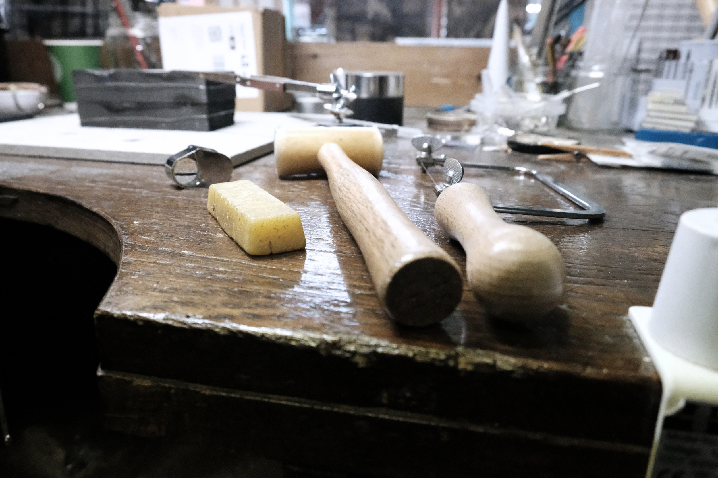 Close-up of a cluttered workbench with woodworking tools, including a mallet, chisels, and clamps, in a workshop setting.