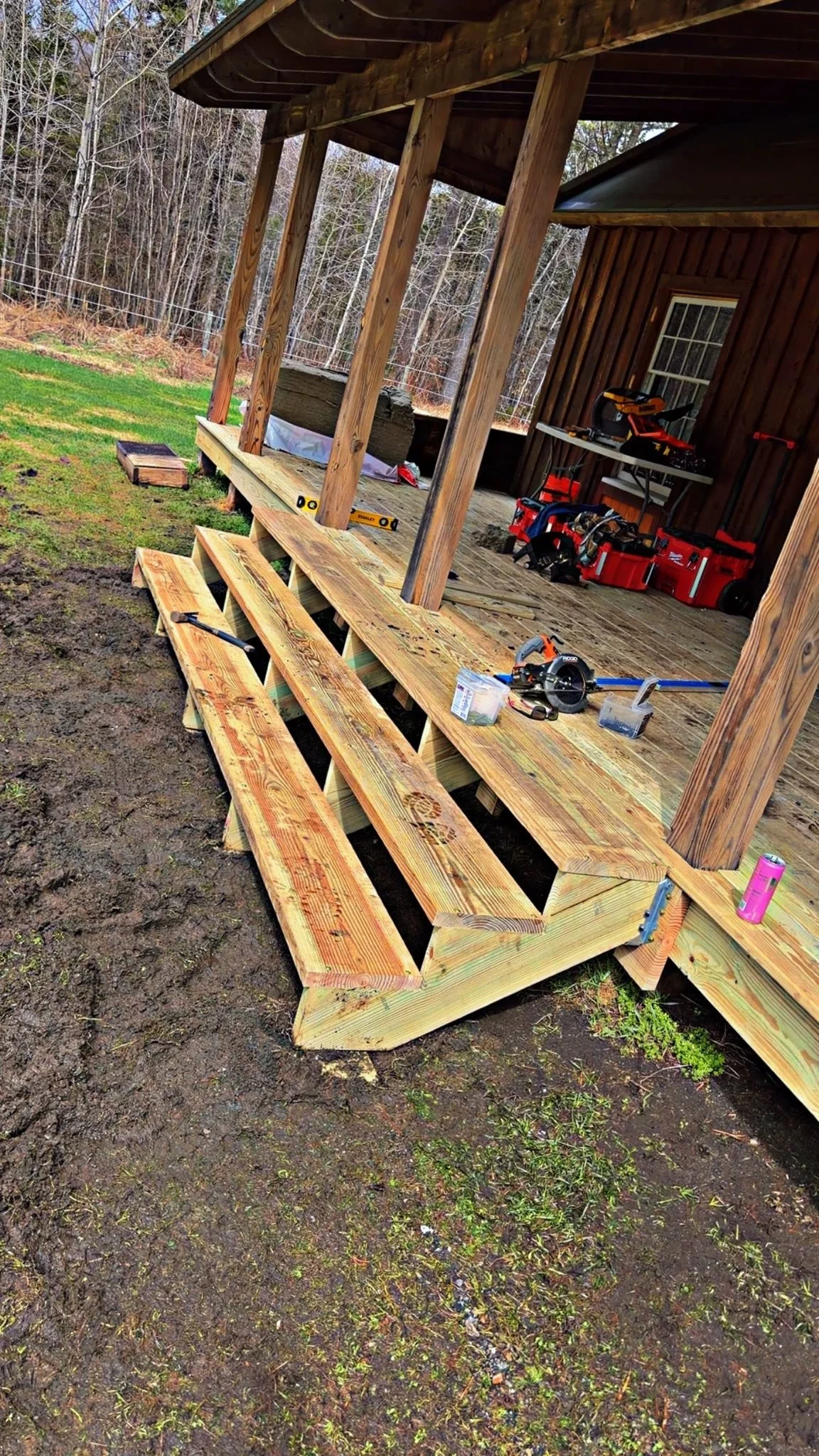 Construction of a wooden porch or deck attached to a house, with tools and materials nearby, in a backyard with bare trees.