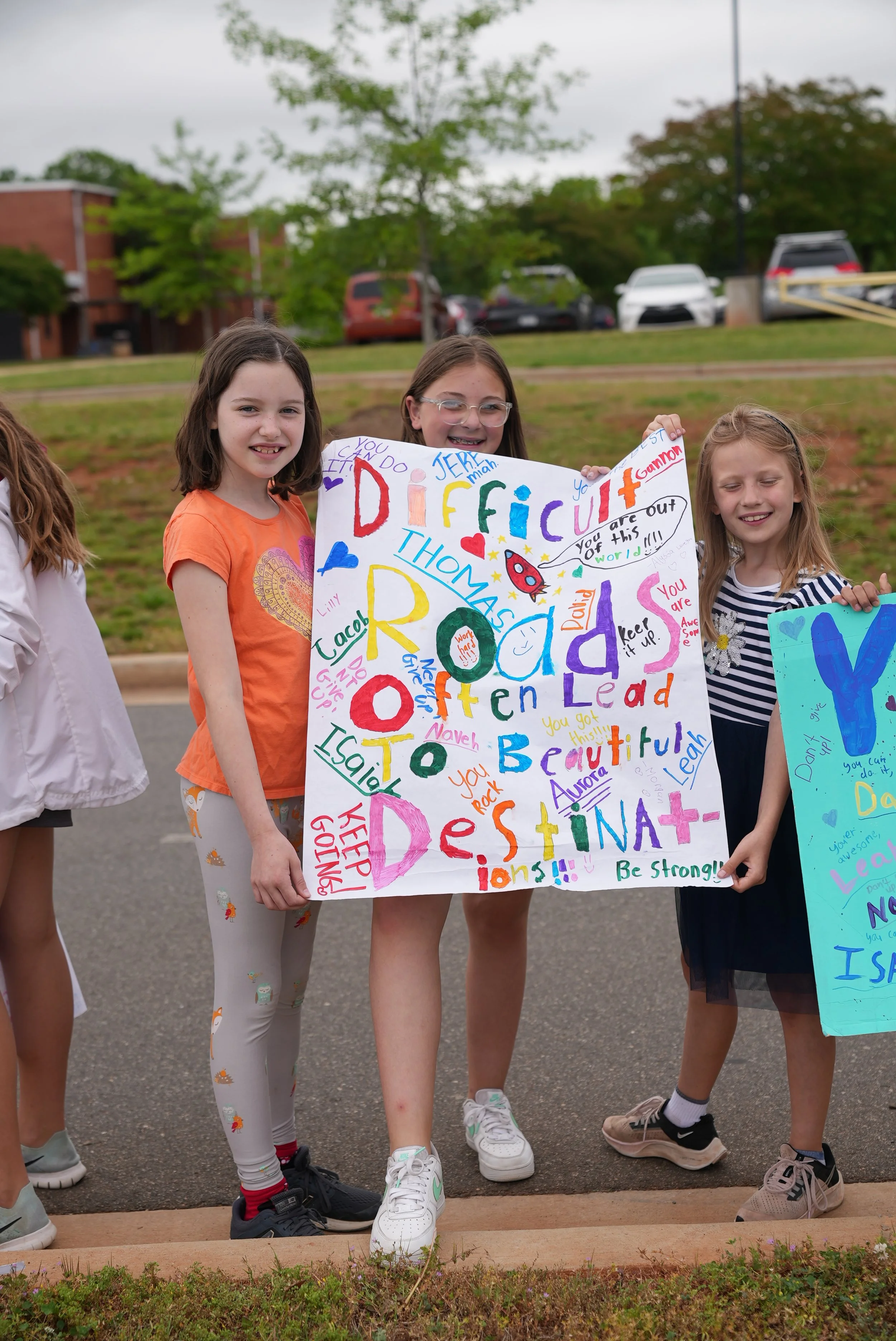 Group of young girls holding a colorful handmade sign that reads "Difficult roads often lead to beautiful destinations!", in support of the Rock Hill Special Olympics event.
