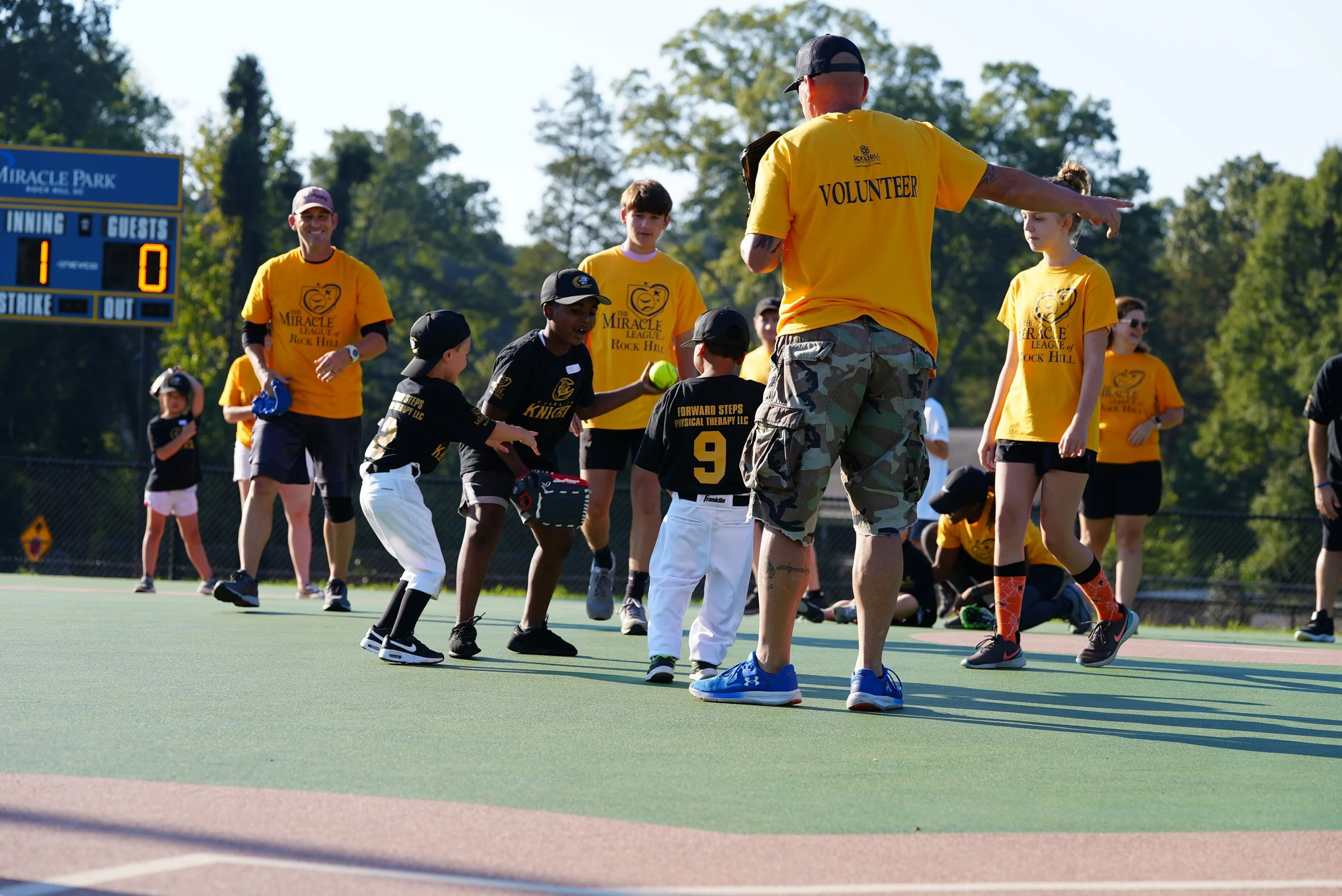 Children and adults playing and engaging in a baseball game on an outdoor field during daytime.