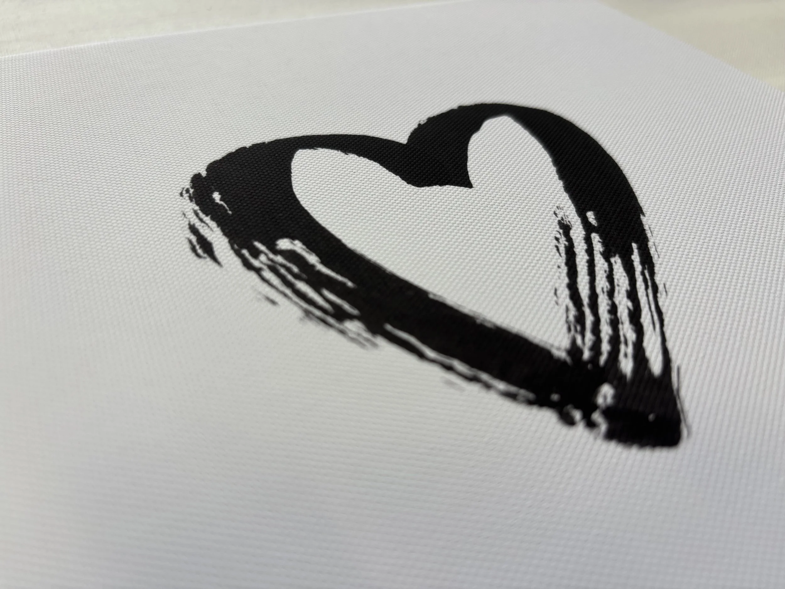 Close-up of a black eye-shaped brushstroke on white textured fabric or canvas.