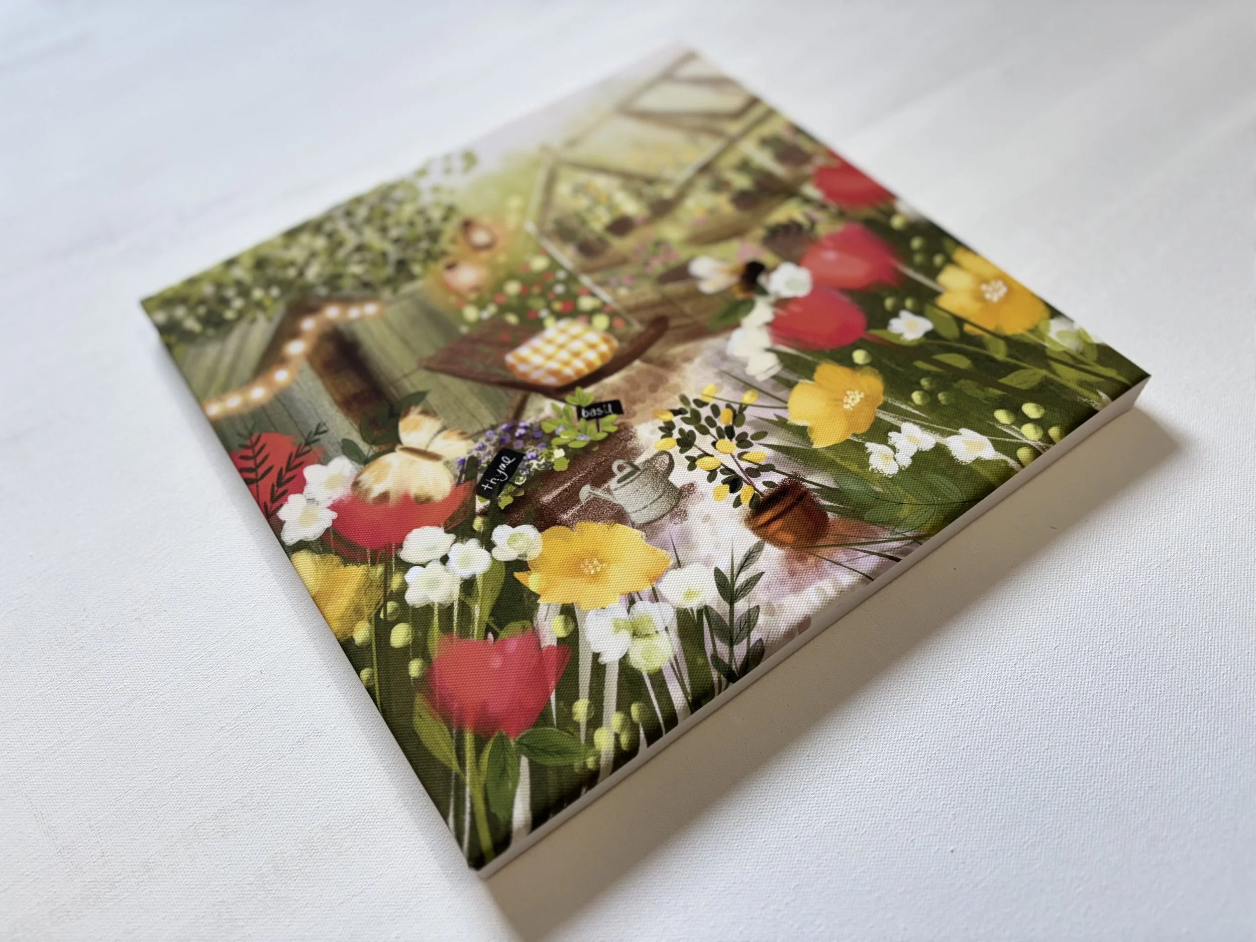 Close-up of a colorful printed notebook or journal with a garden scene on the cover, featuring flowers, greenery, and a garden table.